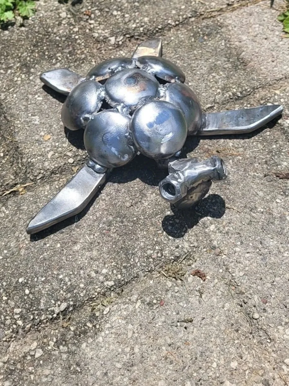Metal sculpture of a turtle lying on a concrete sidewalk.