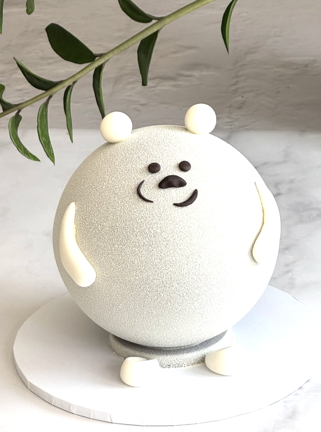 A cake designed to look like a cute white bear with small chocolate facial features, white ear-like decorations, and sitting on a white cake board.