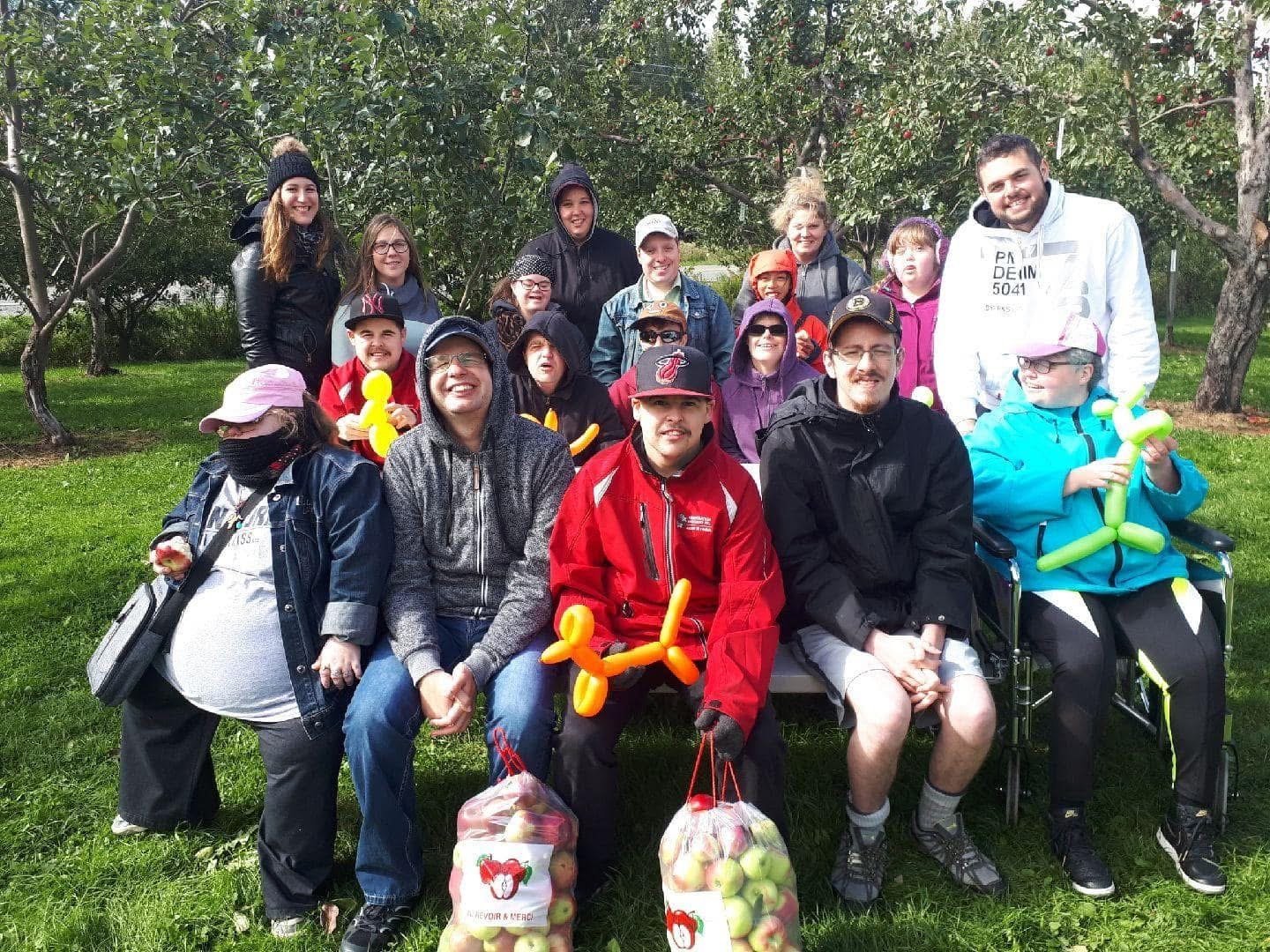Un groupe de personnes souriant et posant dans un verger avec des ballons et des sacs de pommes.