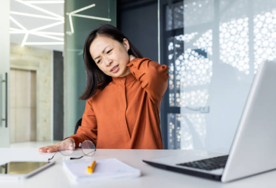 Woman experiencing neck pain at her desk in an office setting.