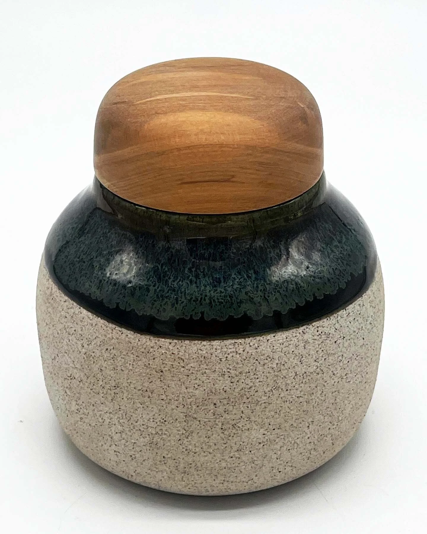 A pet pot with a rounded beige ceramic base, a black and gray section, and a wooden lid.