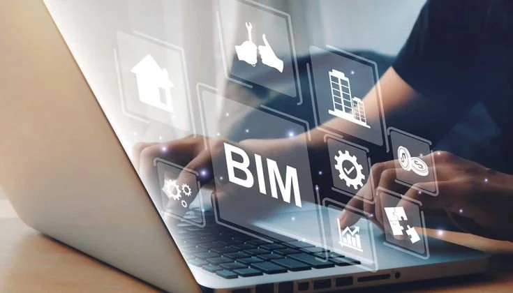 Person using a laptop with holographic icons related to Building Information Modeling (BIM) projecting from the screen.