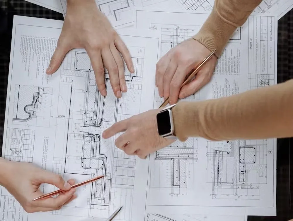 Three people discussing architectural blueprints on a table with tools and papers.