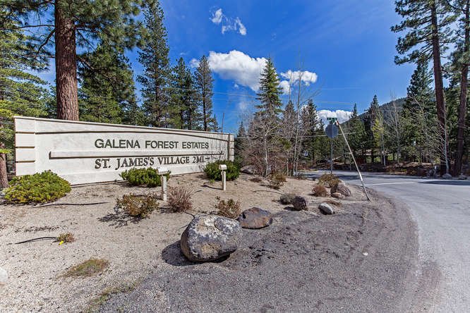 Entrance sign for Galena Forest Estates and St. James' Village, with a gravel road and trees in the background under a partly cloudy sky.