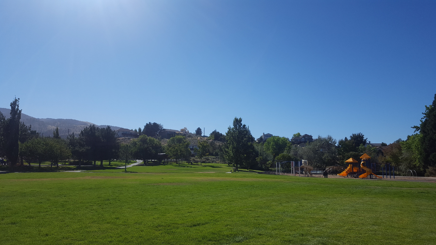 Foothill A park with green grass, trees, and a playground with orange slides under a clear blue sky