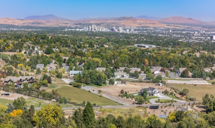 Holcomb Ranch A panoramic view of a suburban neighborhood with houses, trees, and roads, with a city skyline and distant mountains in the background.