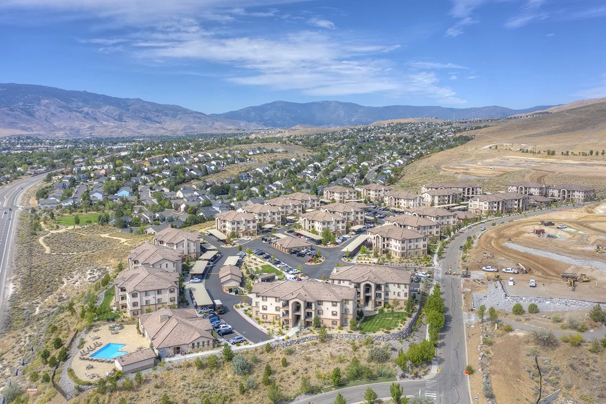 Keystone Aerial view of a residential area with multiple apartment buildings, a swimming pool, parking lots, and nearby construction site with dirt and construction vehicles, surrounded by hills and mountains in the background.