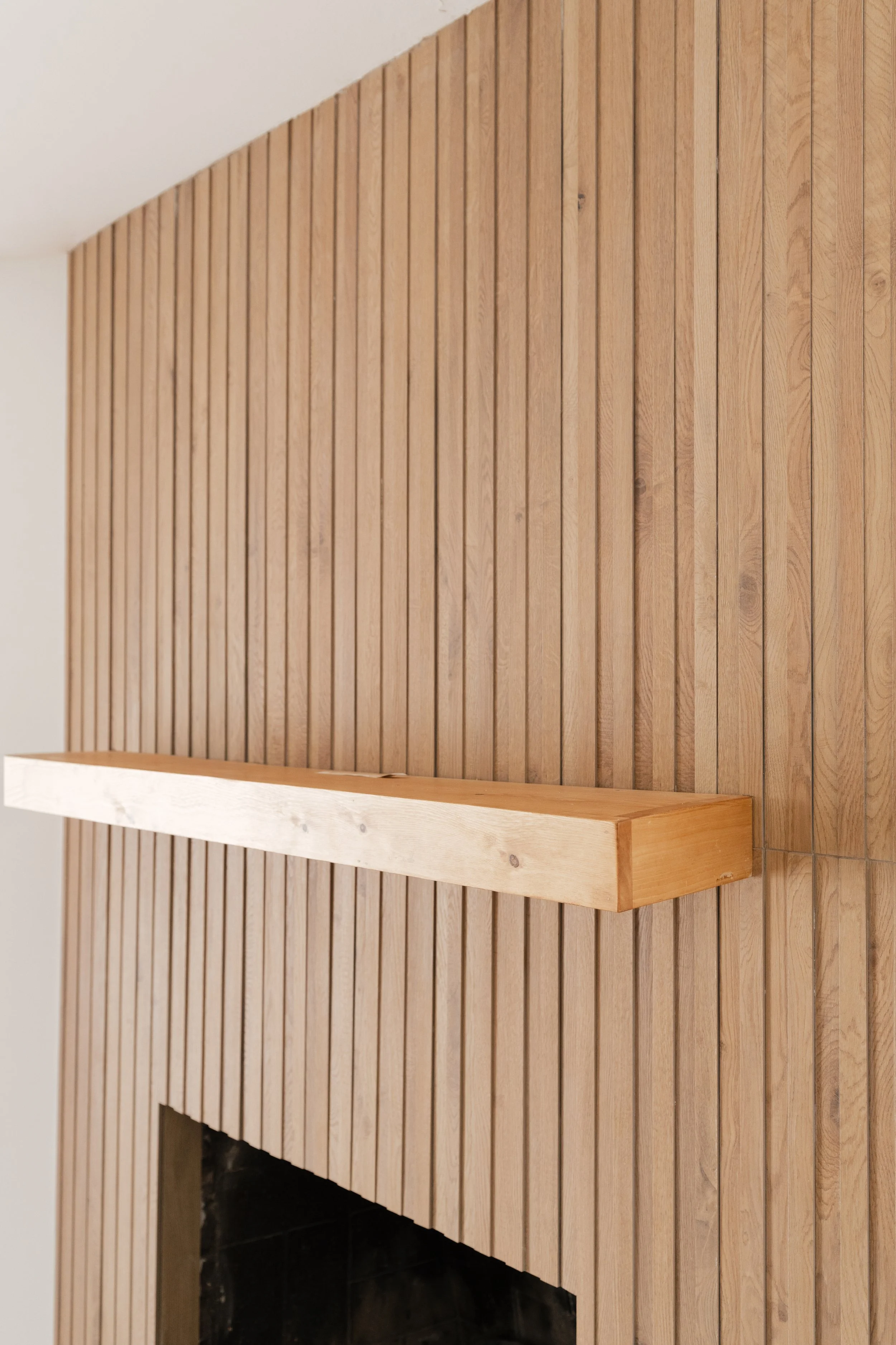 Close-up of a wooden fireplace surround with vertical wood paneling and a wooden mantel.
