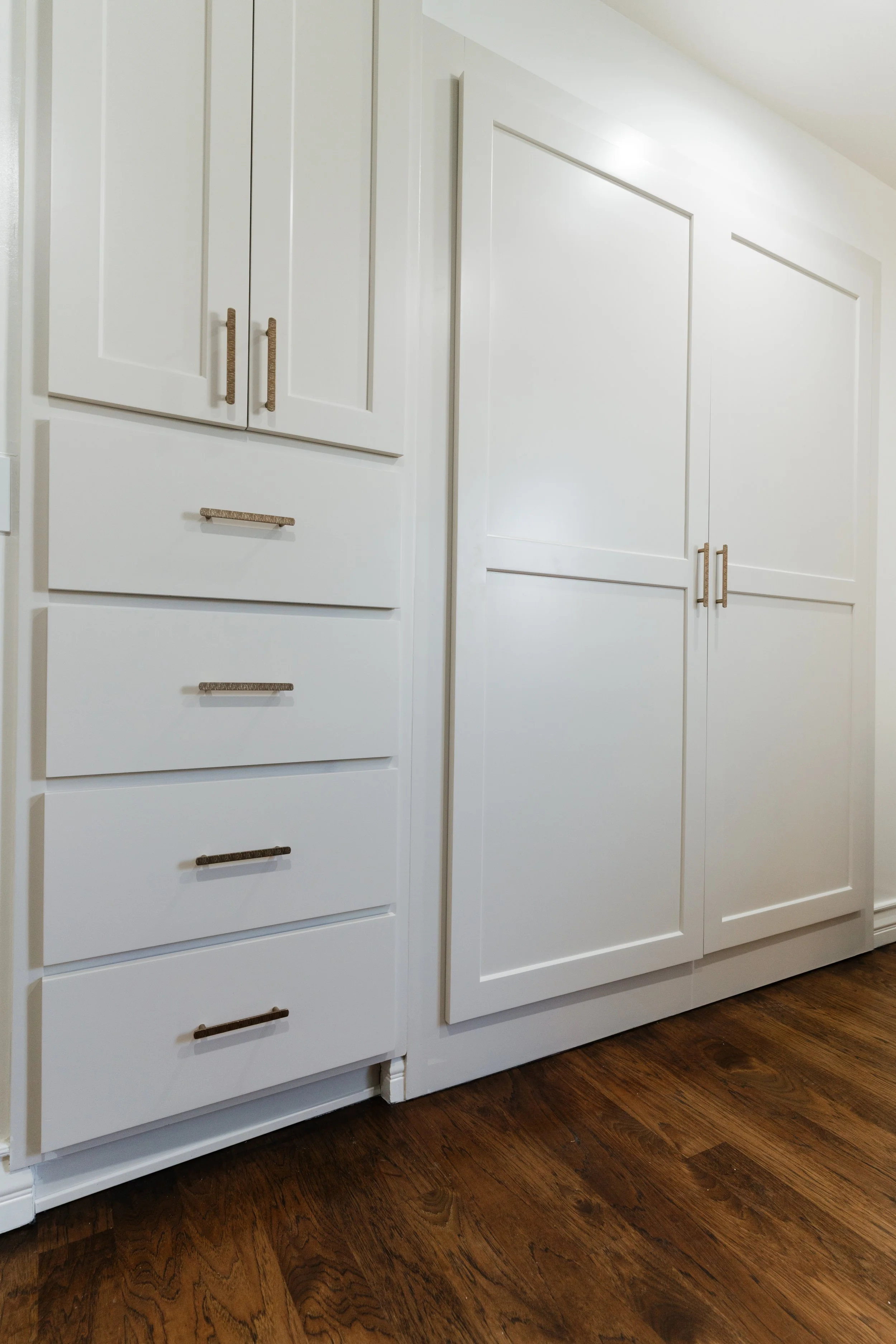 White kitchen cabinets with gold handles, set against a wooden floor.