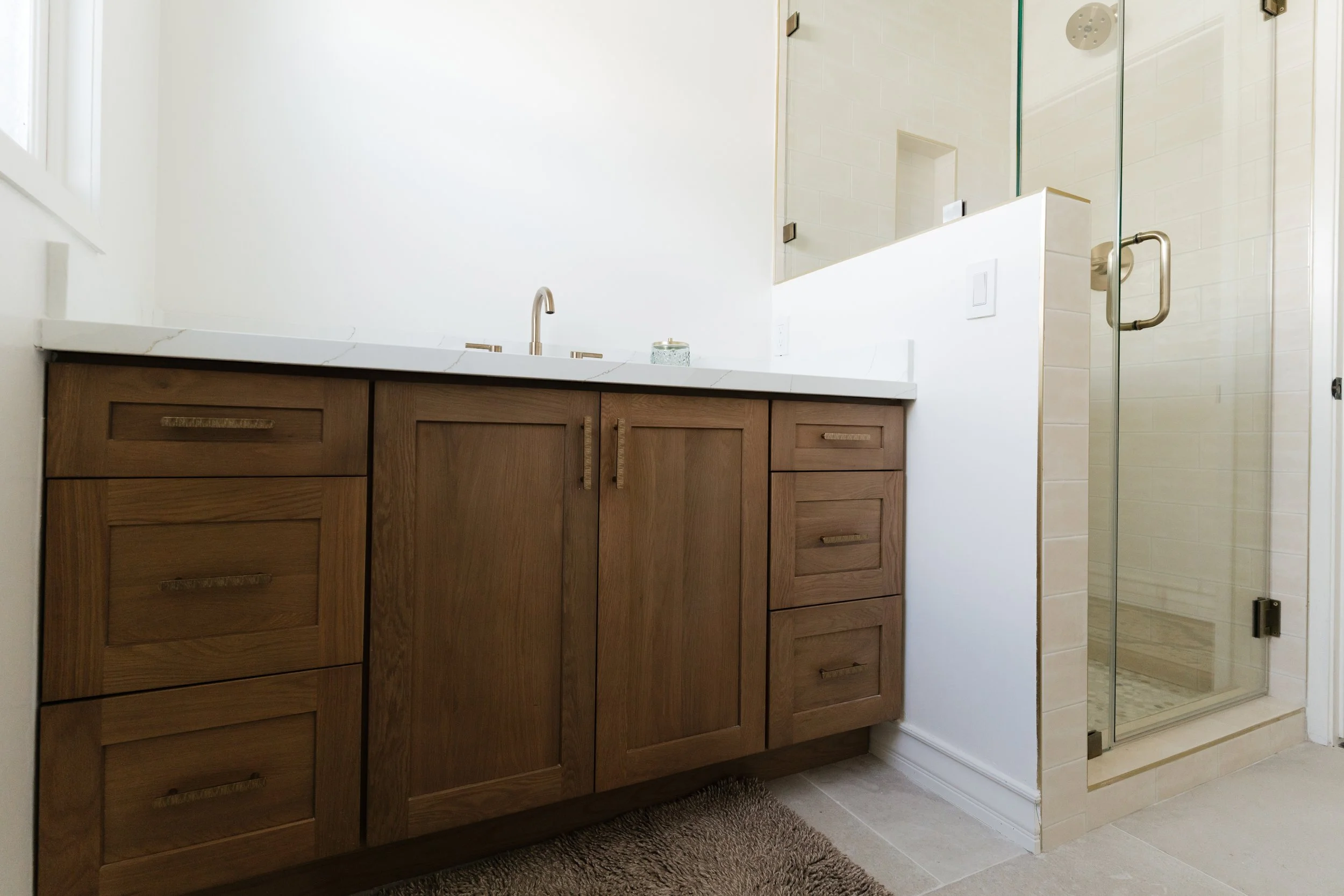 Bathroom with a white oak wooden vanity, white marble countertop, and a glass shower enclosure.