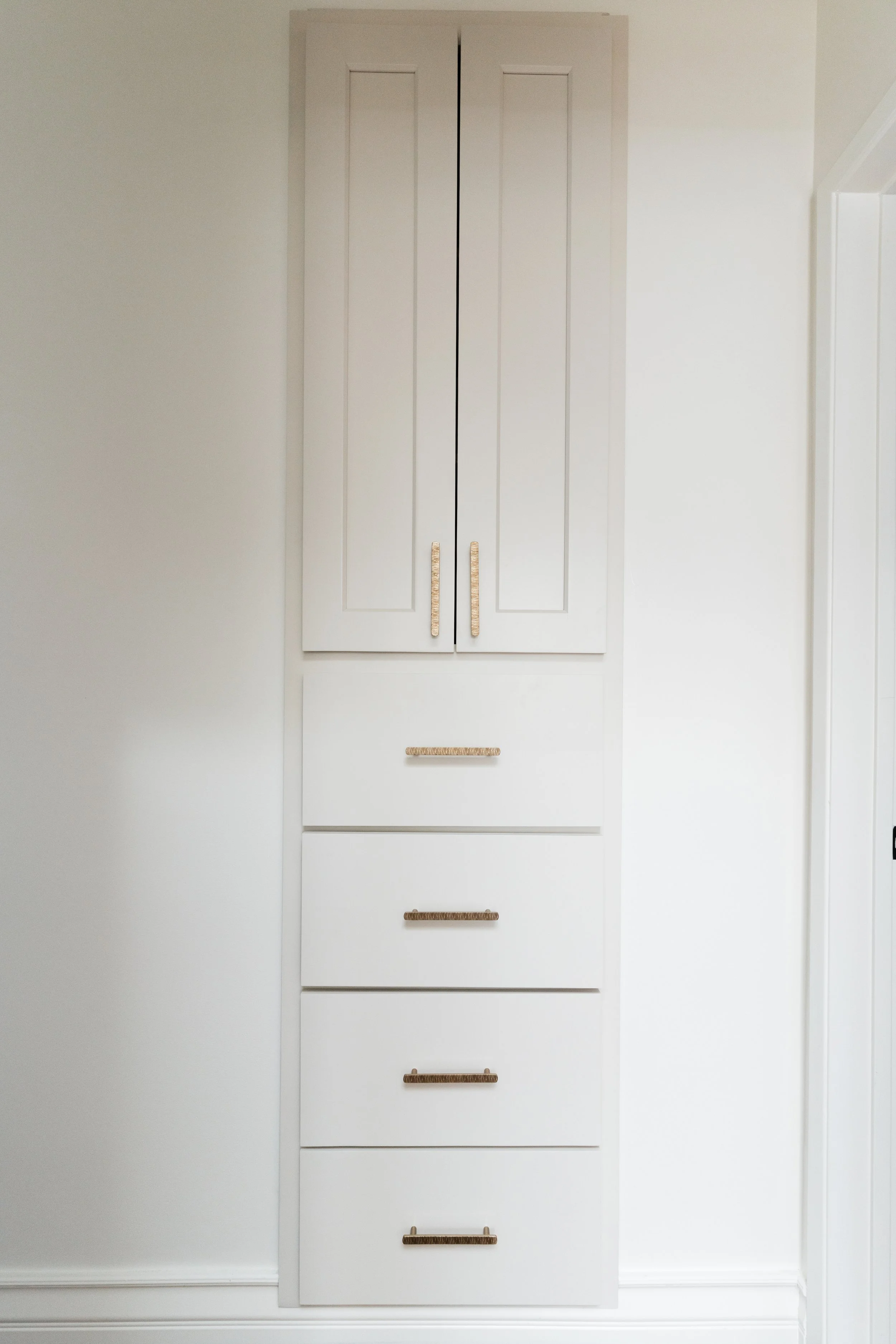 White built-in cabinet with four drawers and two doors, all with wicker handles, installed in a corner of a room with white walls.