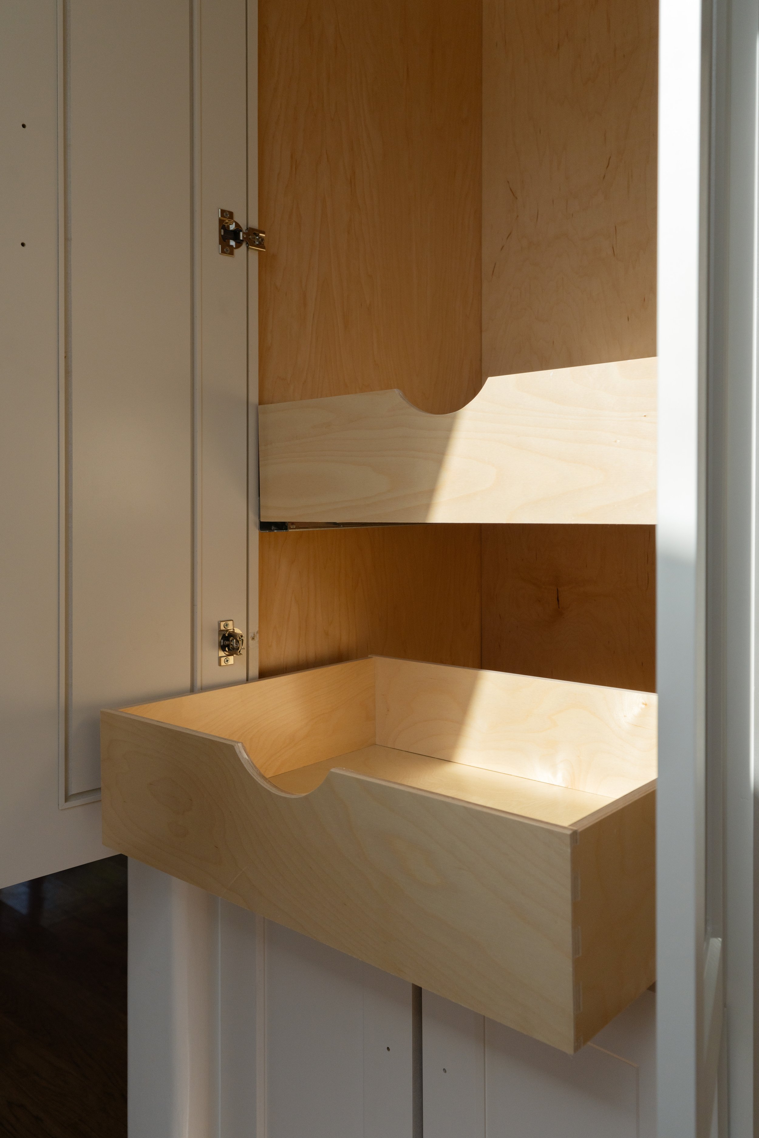 Custom made built in pantry with pull out drawers, a light wood interior and a double matching shelf above it.