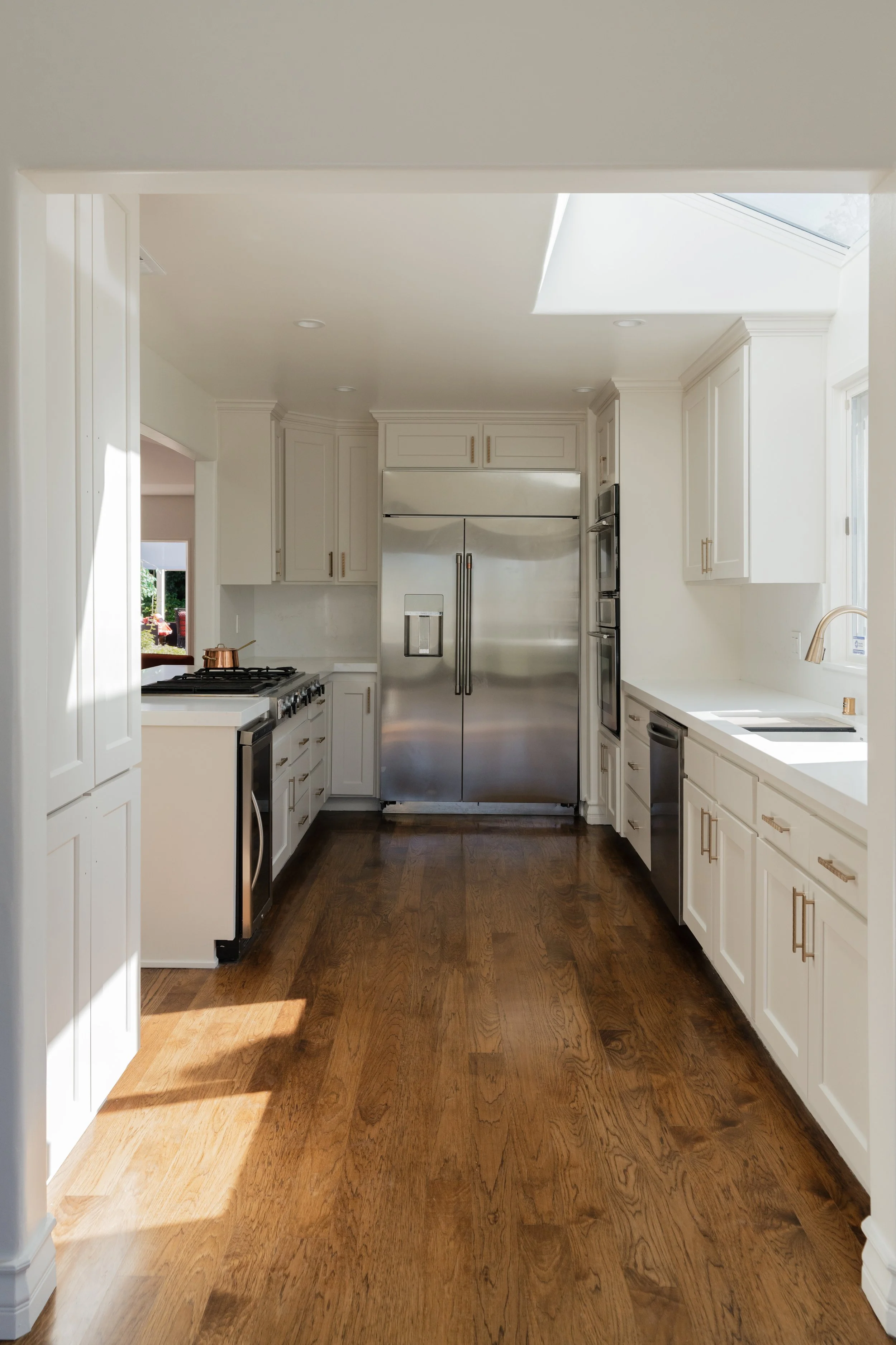 Modern kitchen with white cabinets, stainless steel appliances, and hardwood flooring, illuminated by natural light from a skylight.