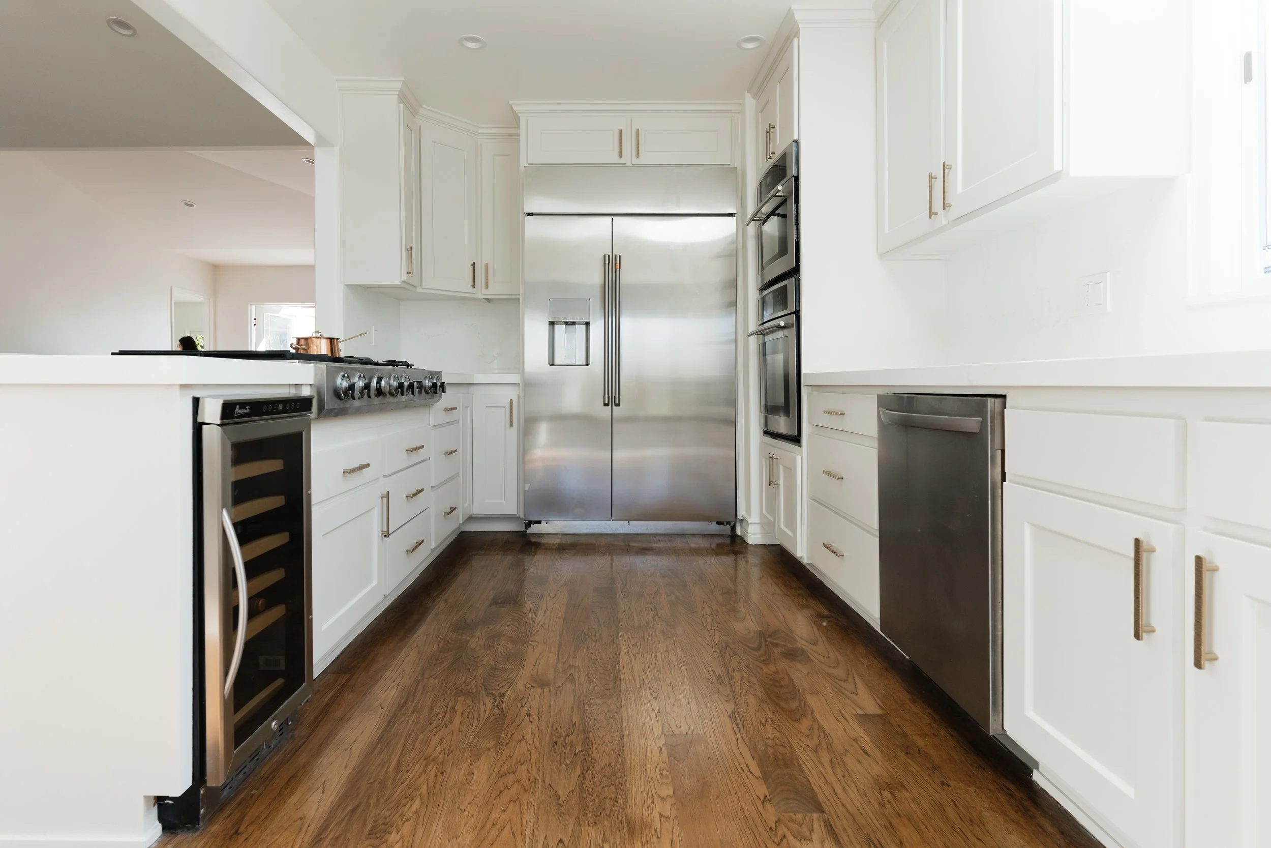 Modern kitchen with white cabinets, stainless steel refrigerator, wall ovens, wine cooler, and hardwood flooring.