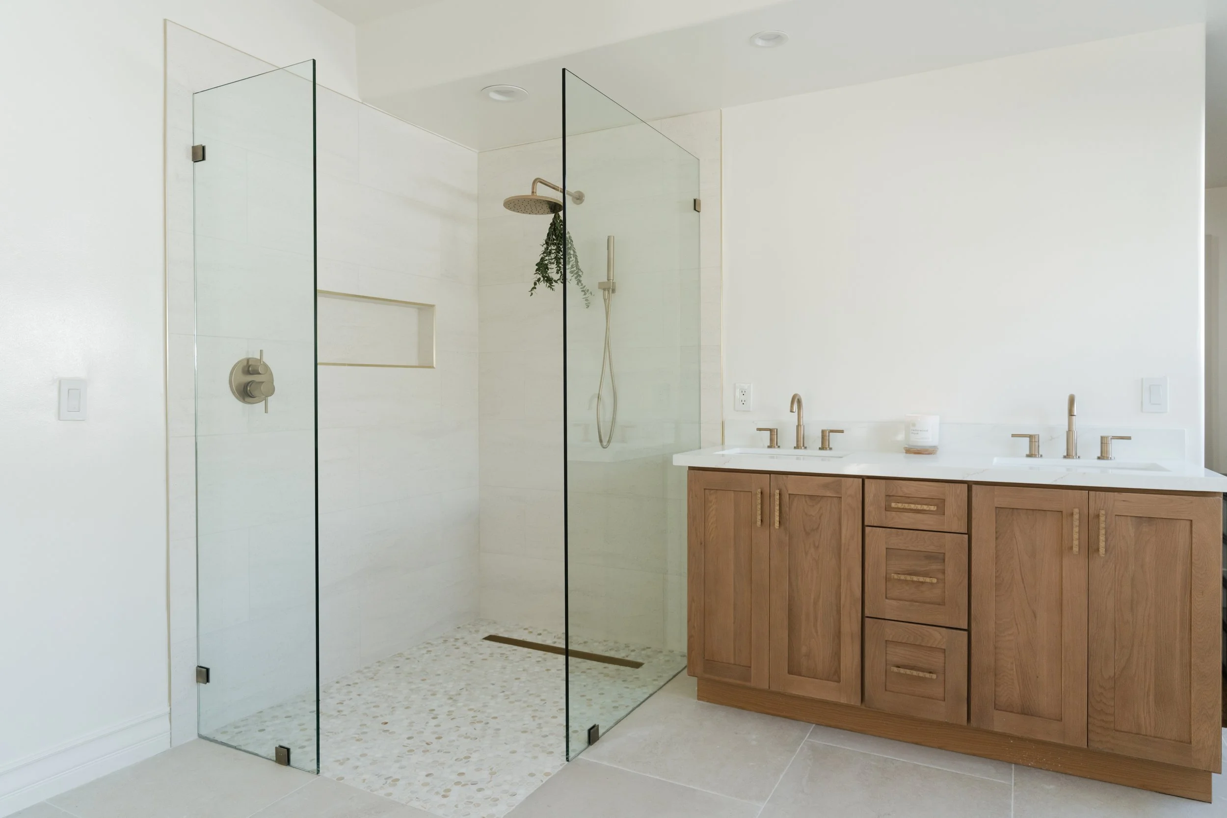 Refinished modern bathroom with a walk in glass-enclosed shower area, wooden vanity with dual sinks, and neutral-colored tiles and walls.