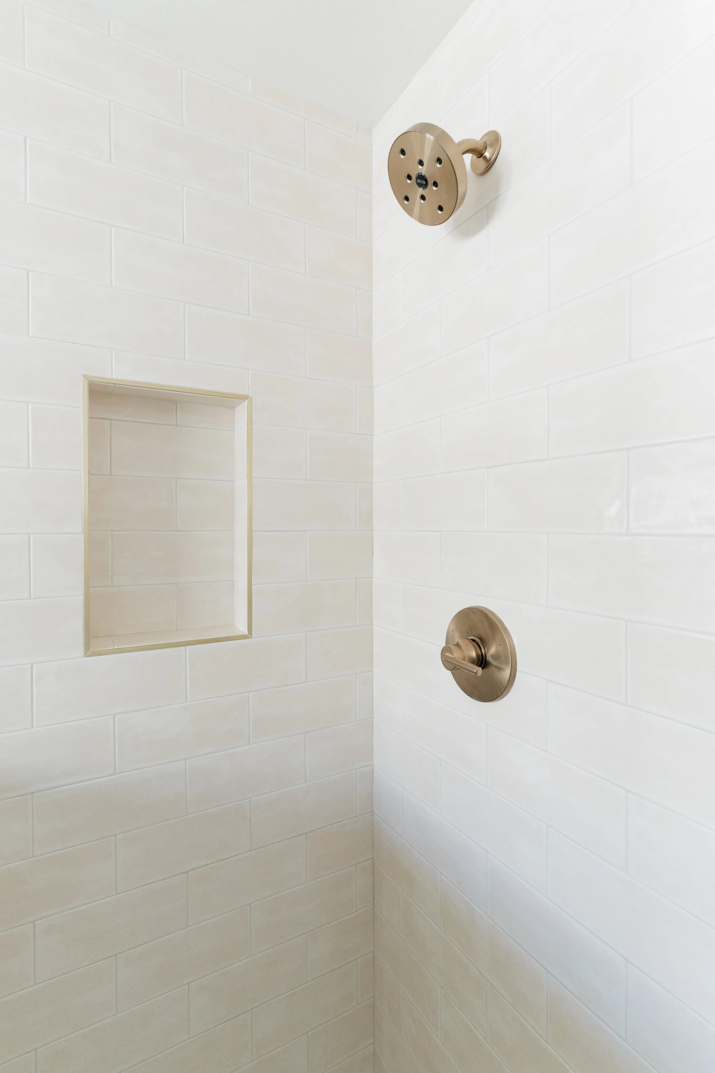 A shower with pink/beige tiles, a champagne gold round showerhead, and a side control handle.