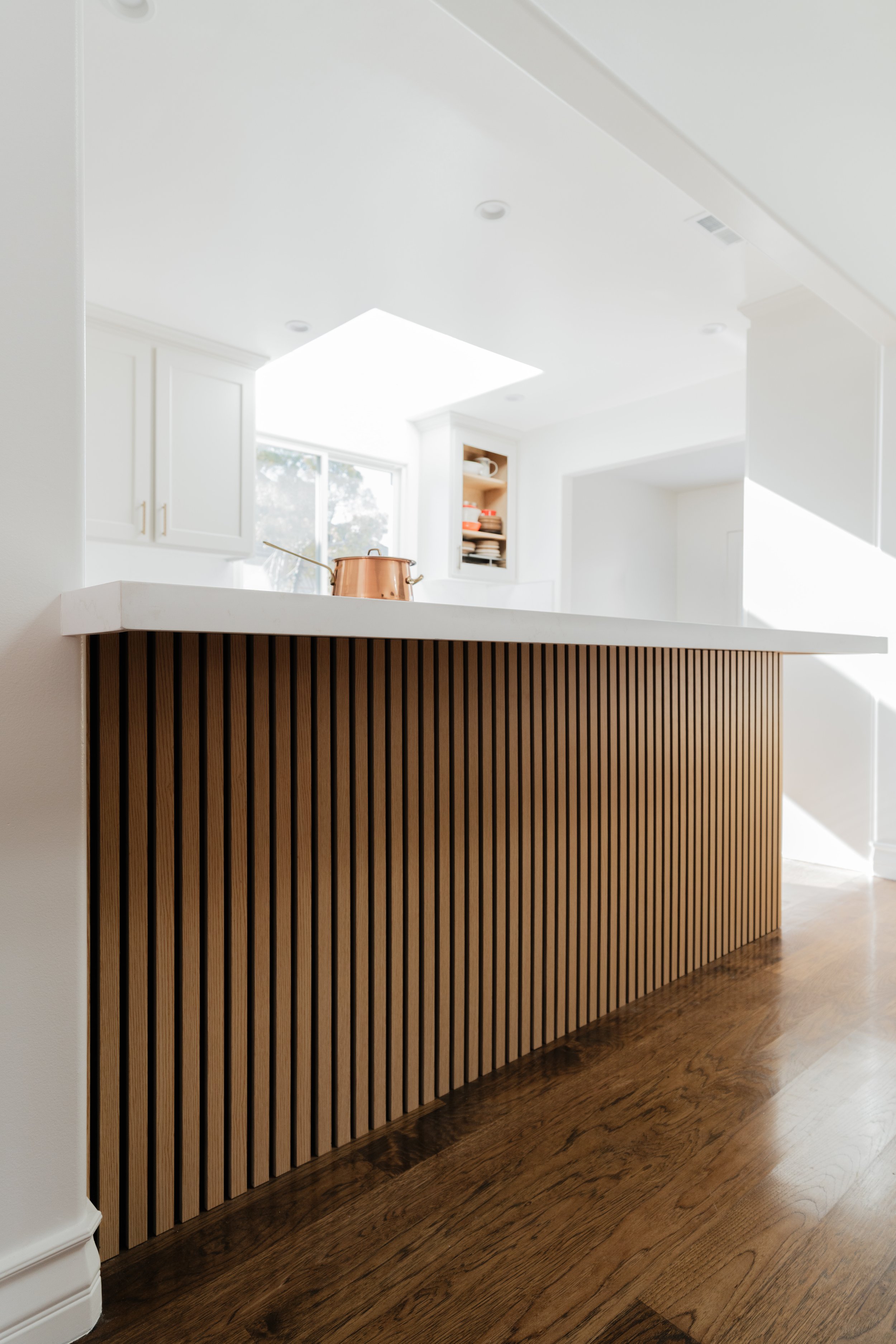 Modern kitchen with white cabinets, a skylight, and wooden slat detail on the island.