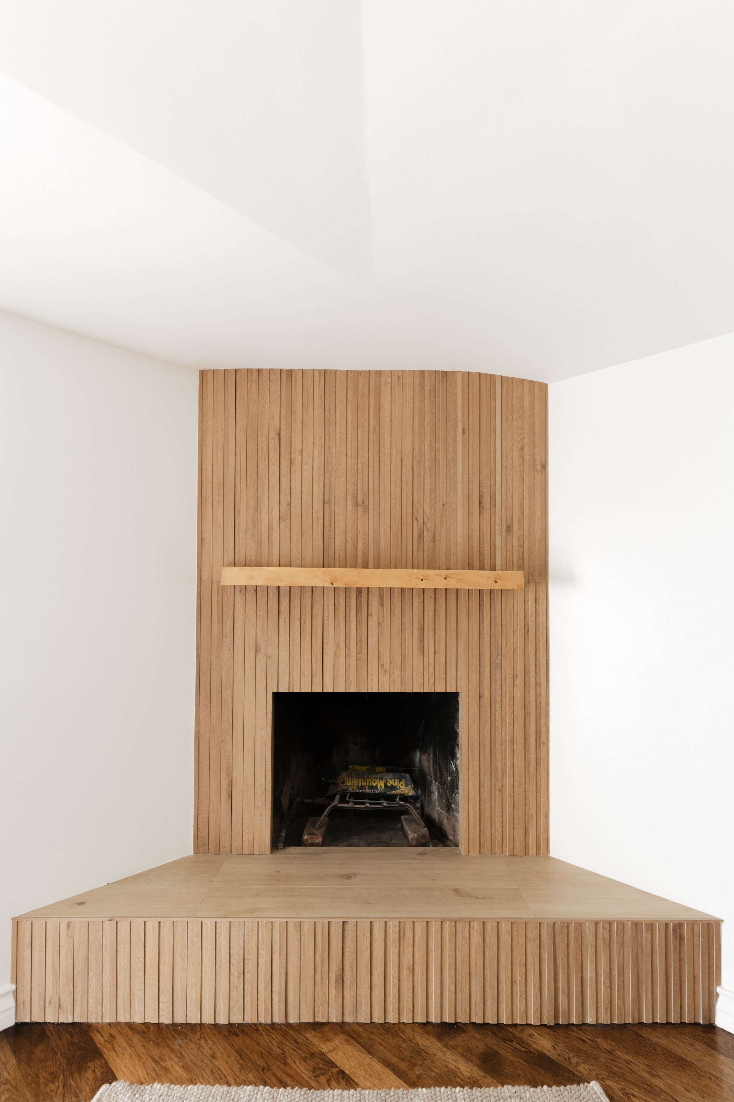 A modern fireplace with a wooden surround and a built-in mantel in a white room.
