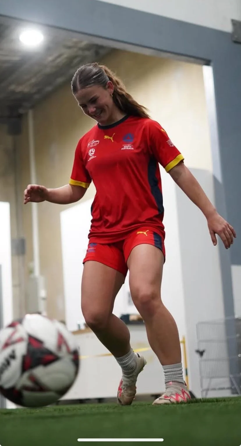 Woman in red sports uniform juggling soccer ball indoors.