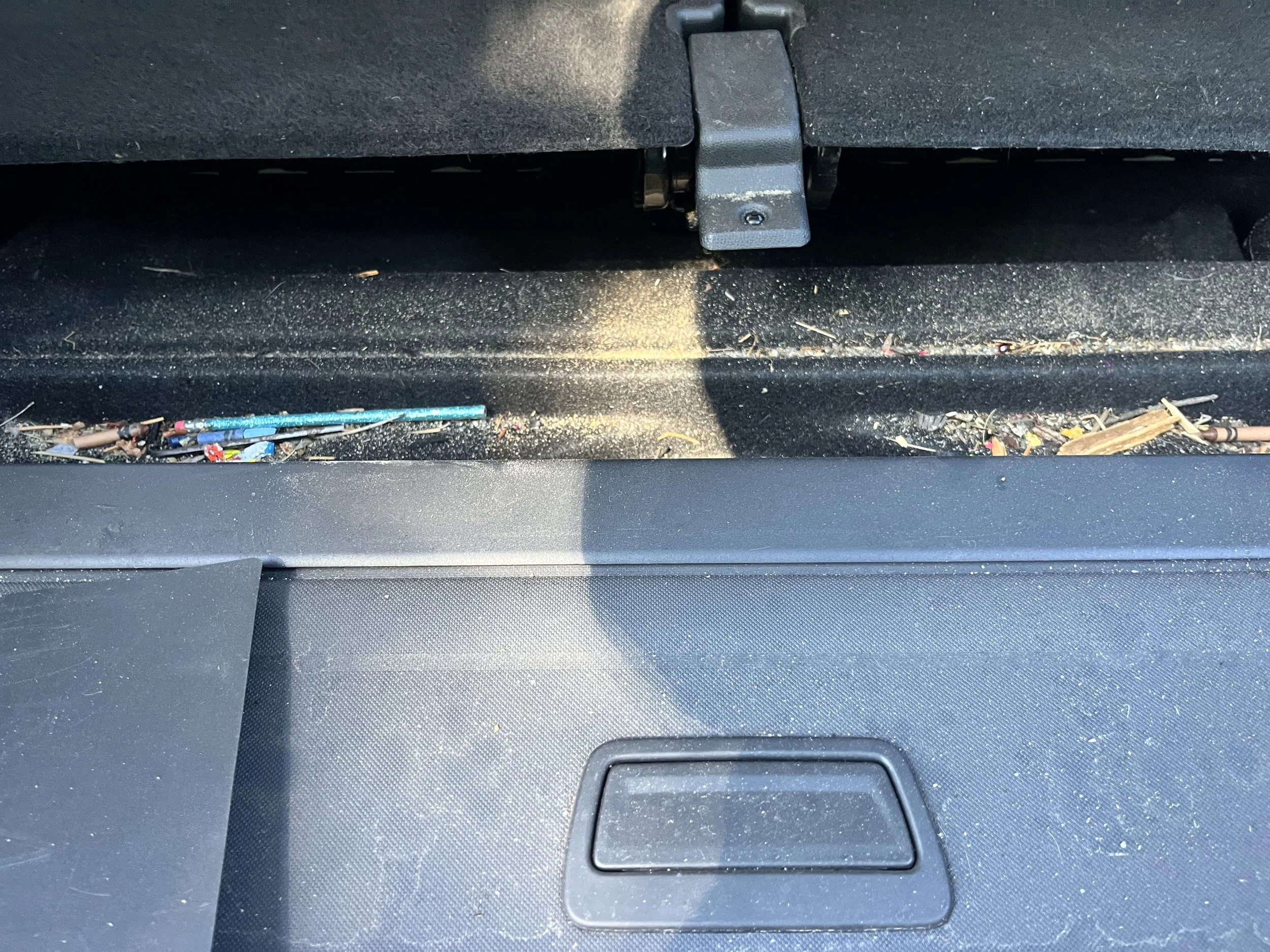 Inside the car's front storage compartment showing dust, debris, and small objects.