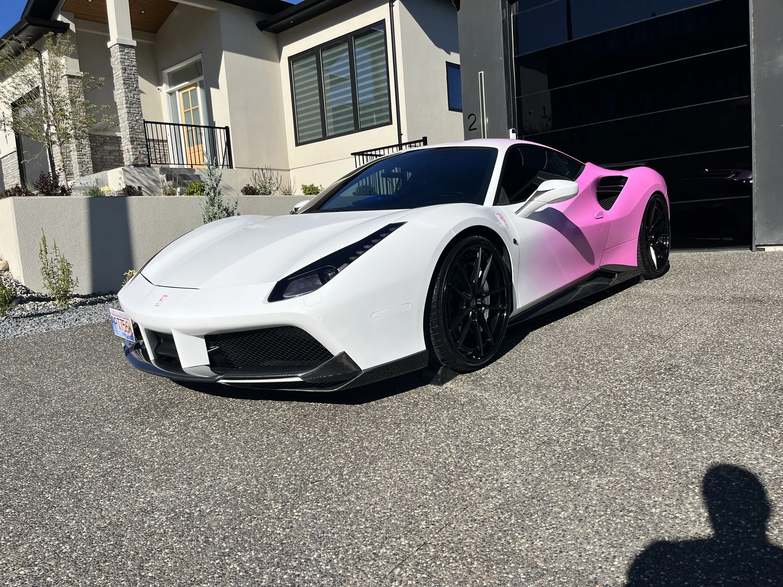 A white and pink sports car parked near a modern residential house with a garage door.