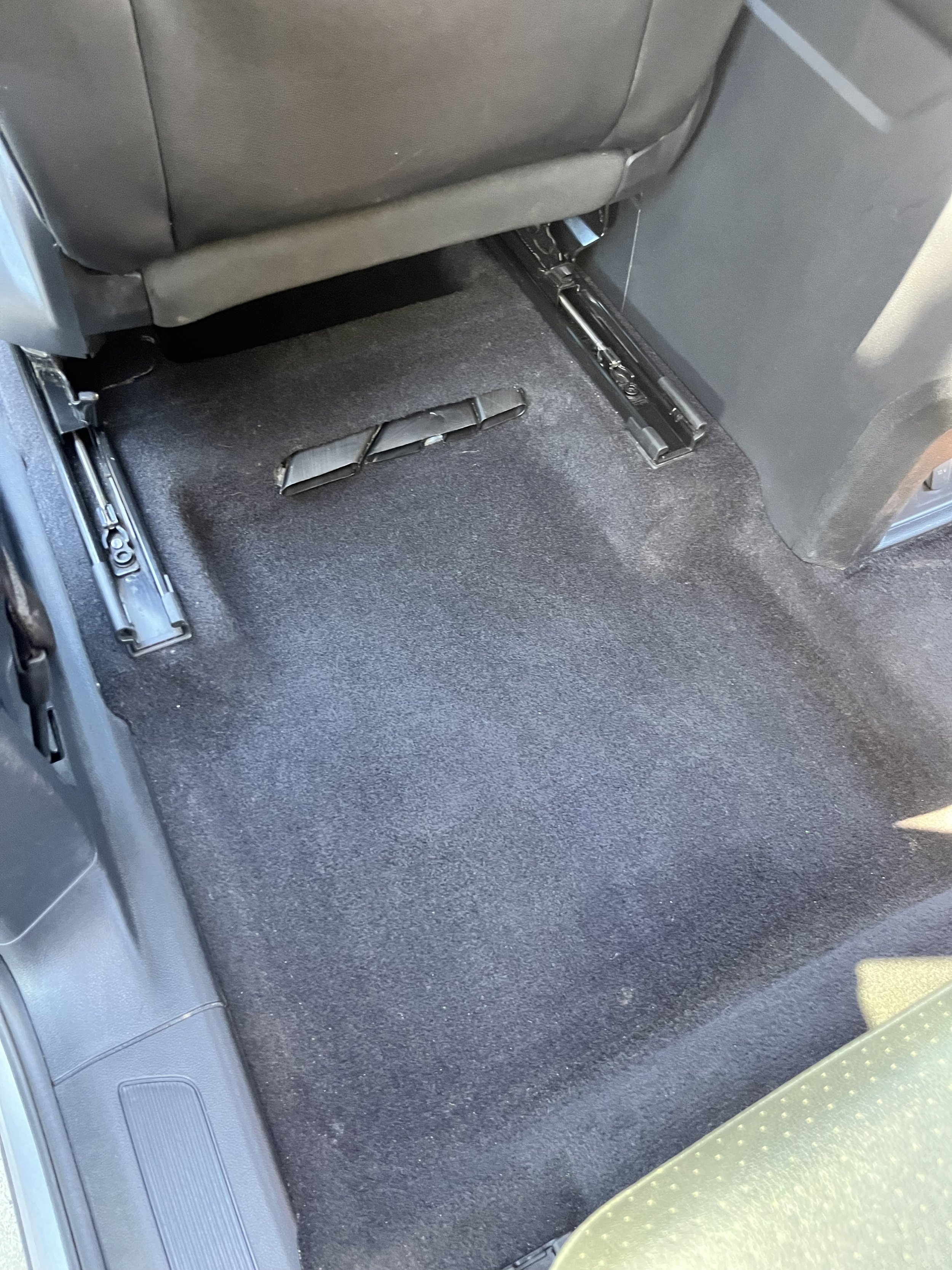 Empty car back seat area with folded seat rails and dark carpet flooring.