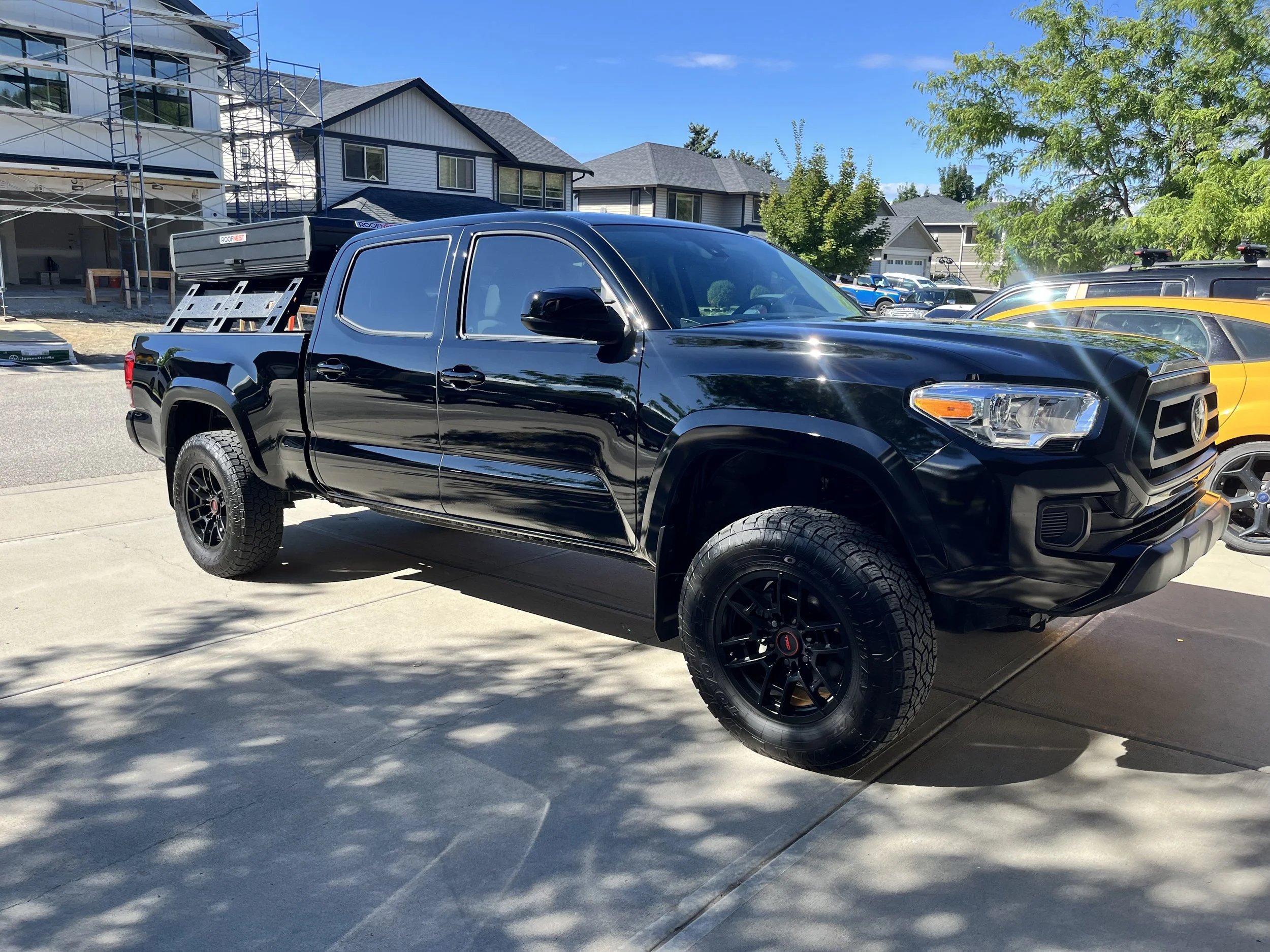 Black pickup truck parked on driveway with housing construction in background and trees casting shadows
