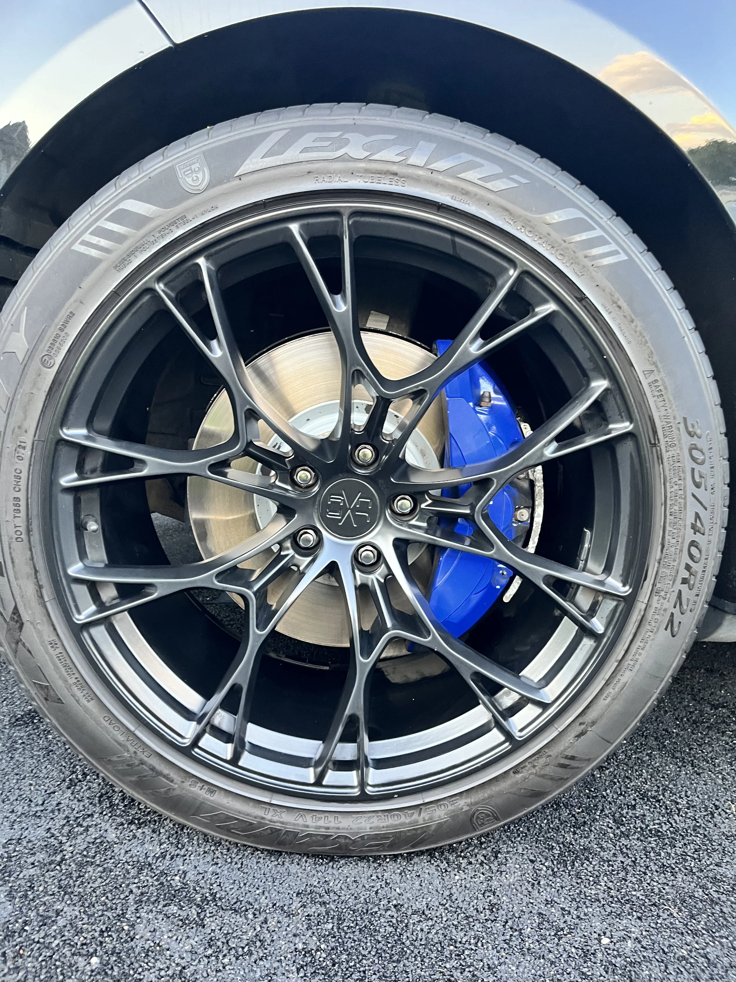 Close-up of a car wheel featuring a metallic alloy rim, a high-performance tire, and a blue brake caliper visible behind the rim.
