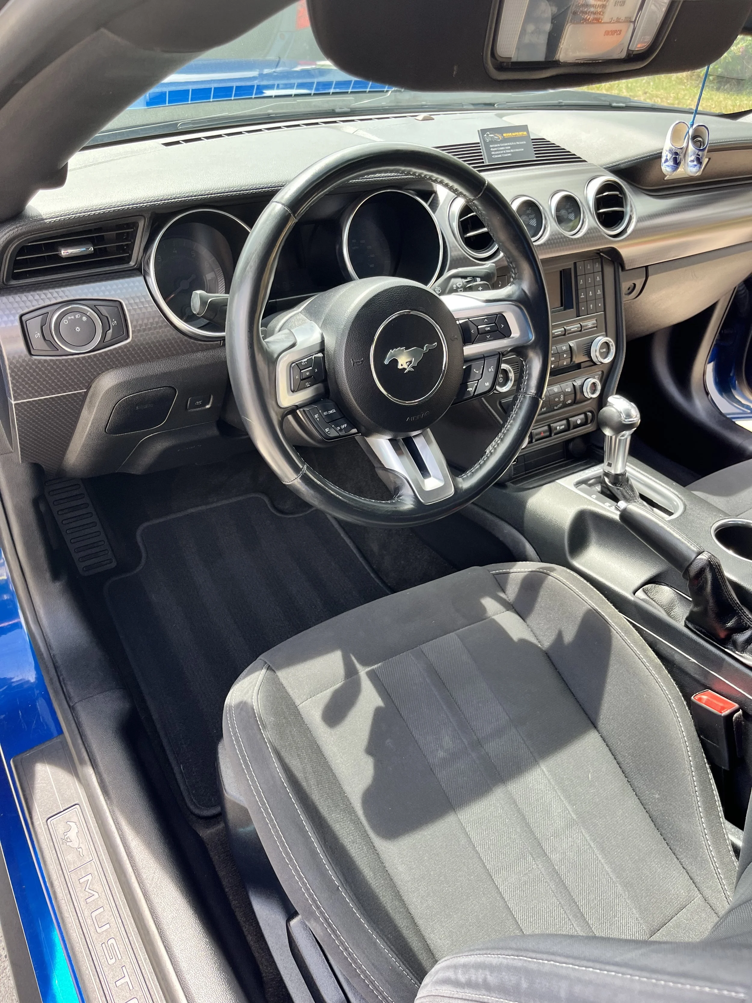 Inside view of a blue Ford Mustang, showing the steering wheel, dashboard, center console, and front seat.