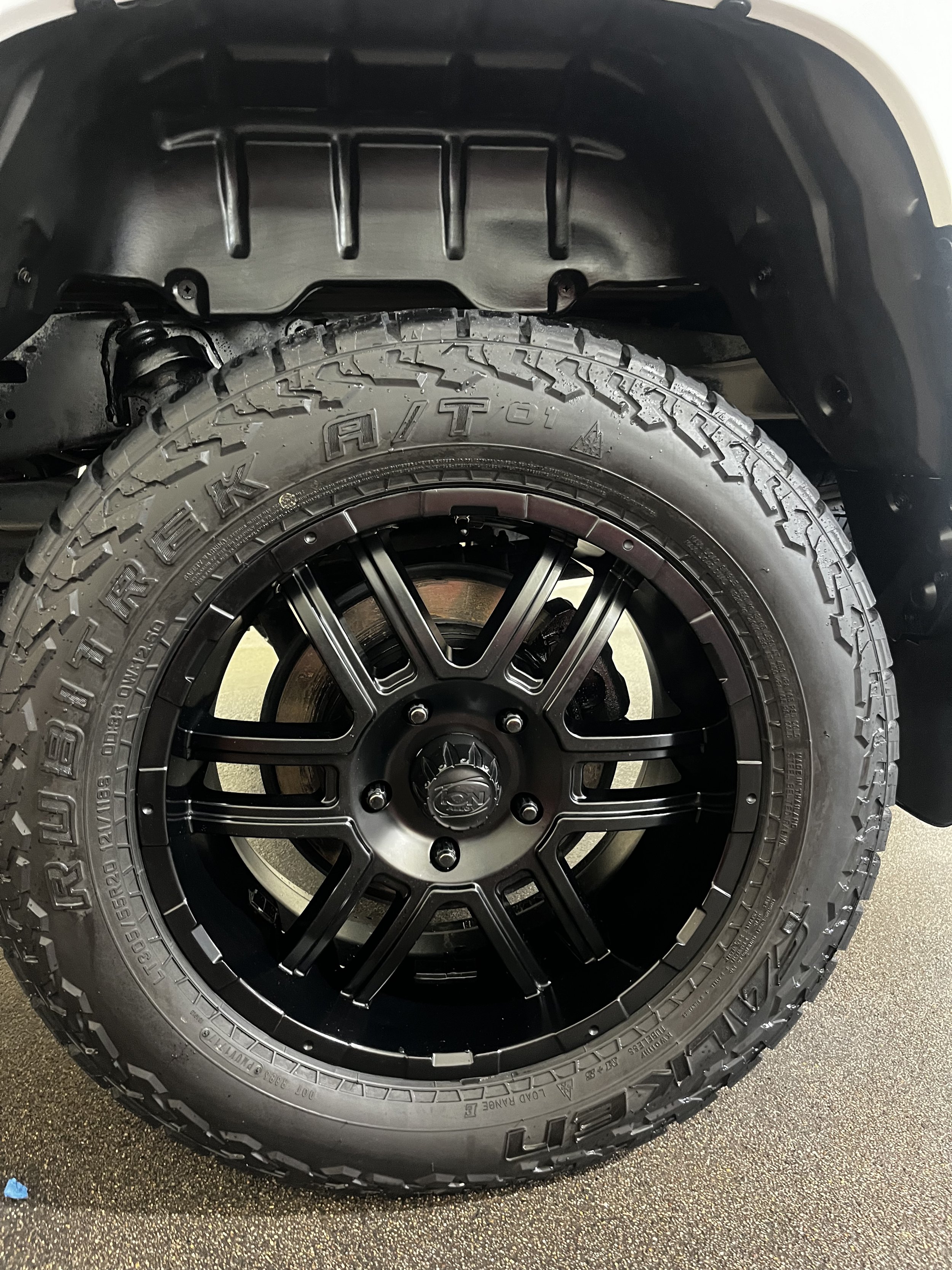 Close-up of a black off-road tire mounted on a black alloy wheel, inside the wheel well of a vehicle.