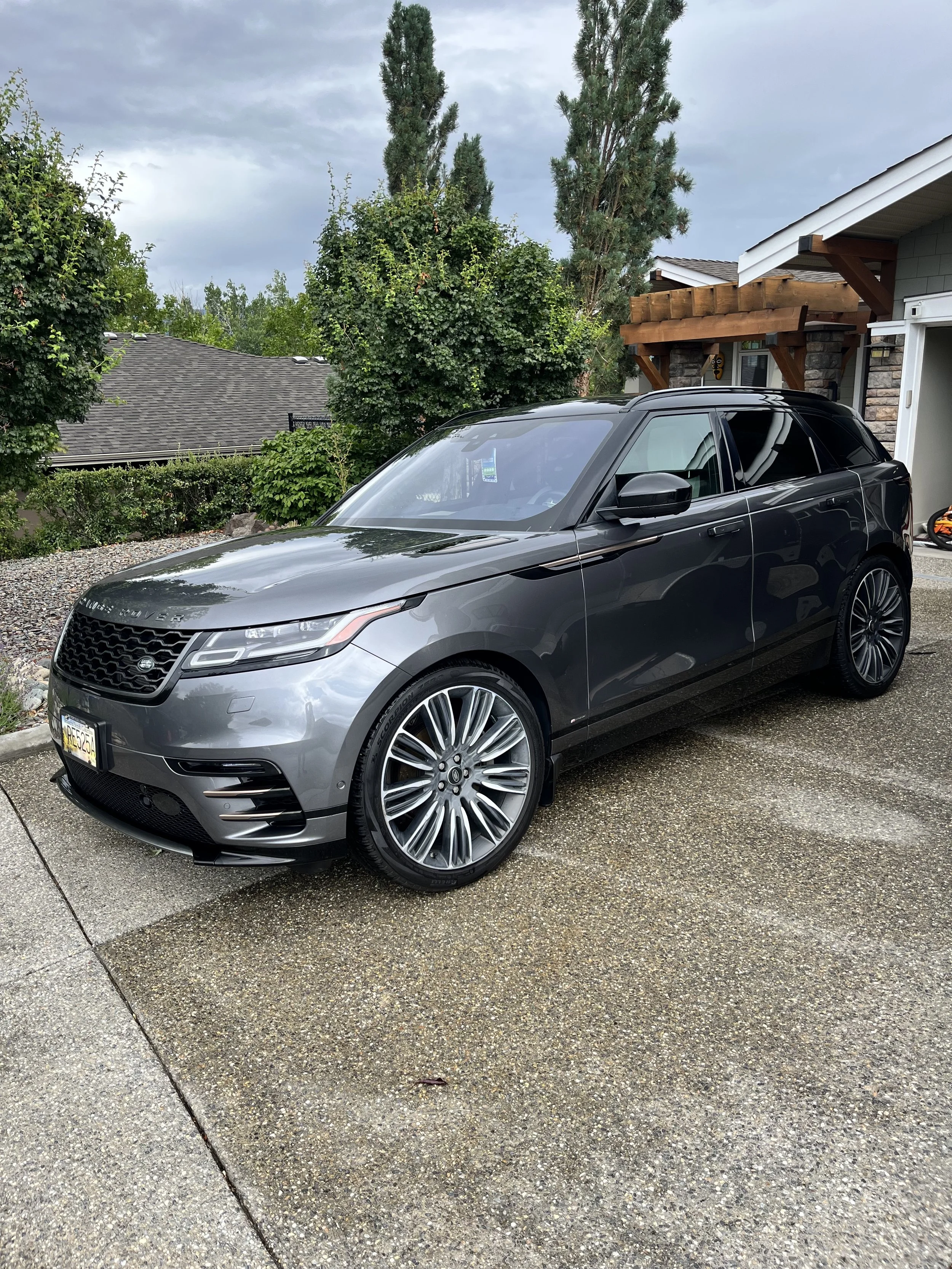 A gray Range Rover SUV parked in a residential driveway with trees and a house in the background.