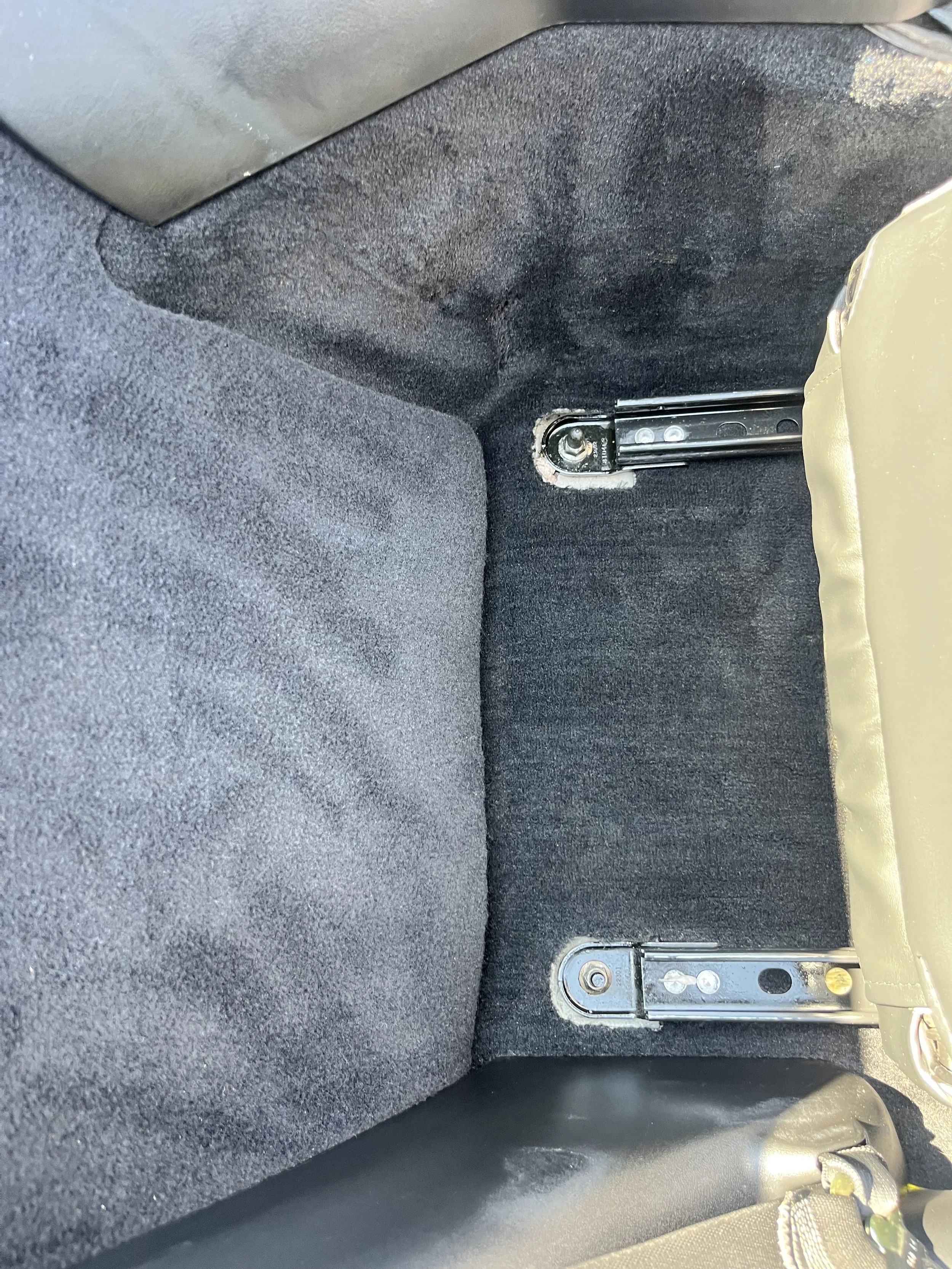 The interior of a car's rear seat area with the backrest removed, exposing mounting brackets for the seat, and the carpeted floor.
