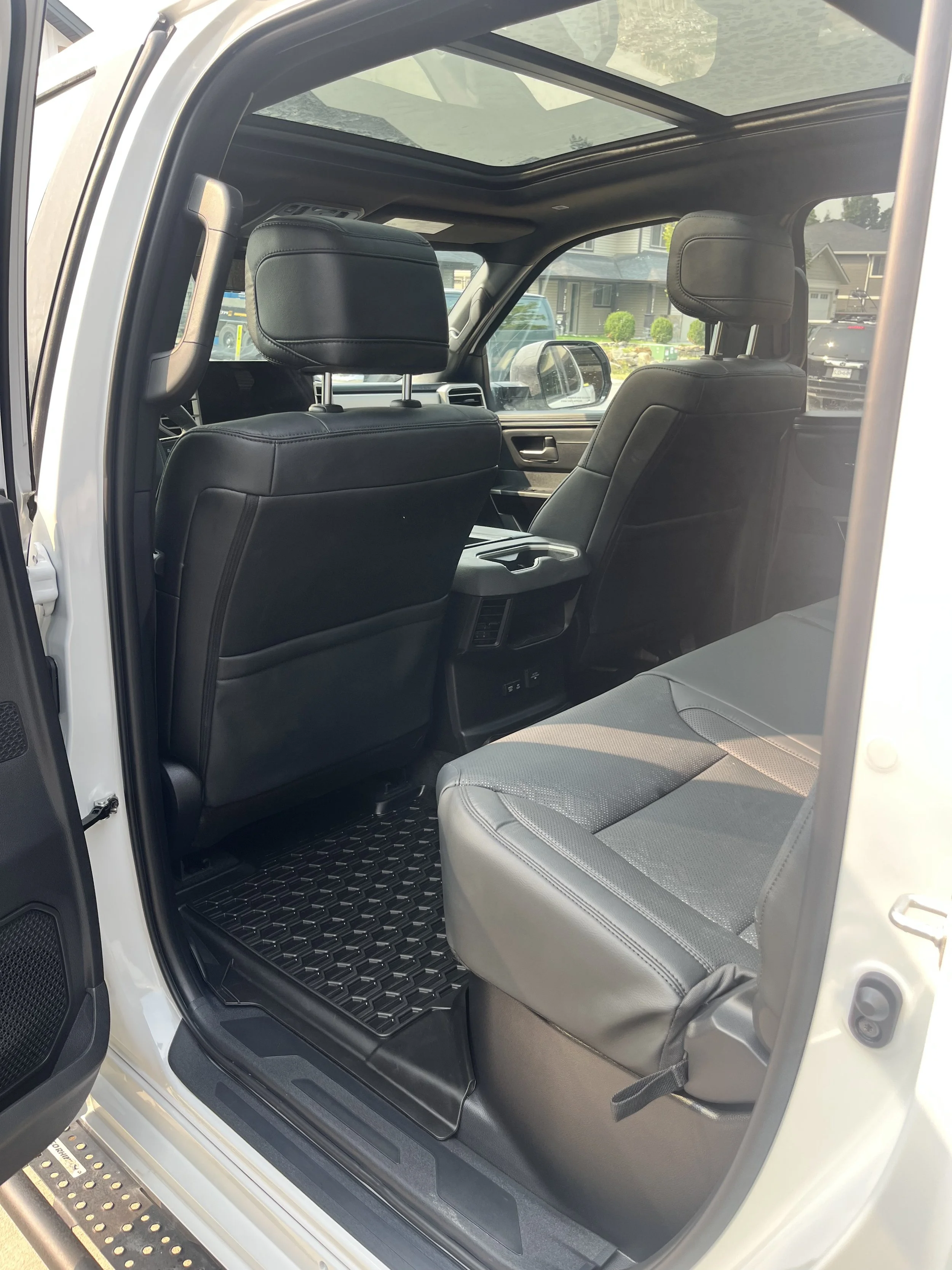 Interior of a vehicle showing black leather seats, a view through the open door, and a sunroof.