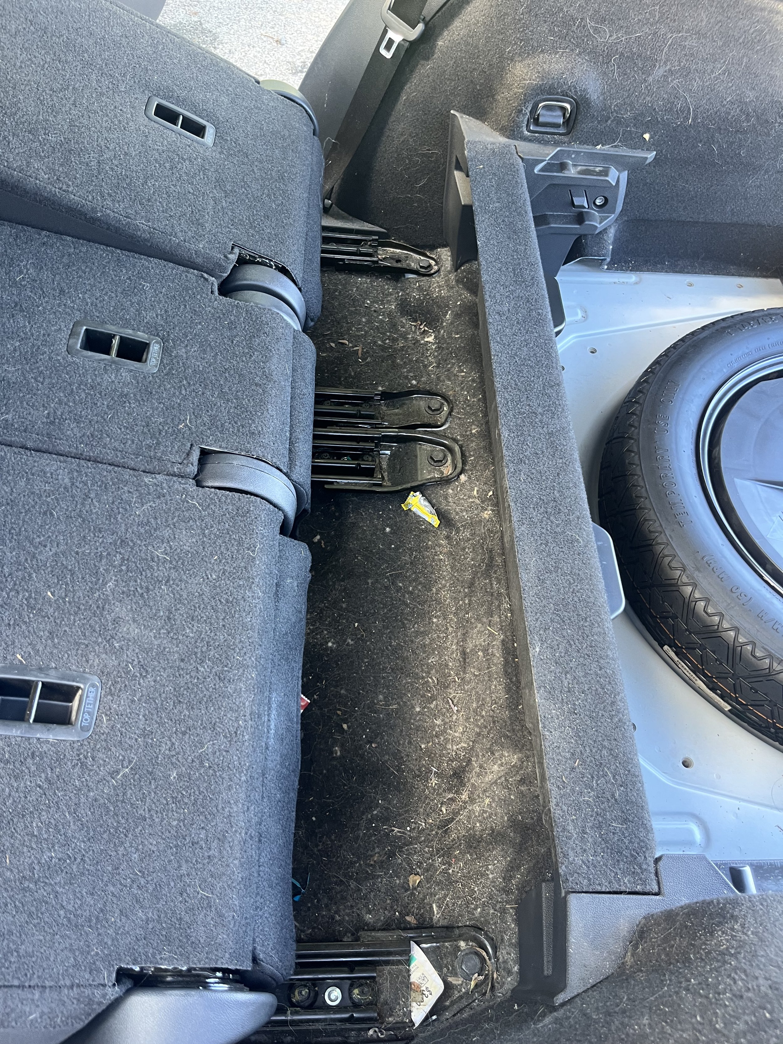 The back of a vehicle with the rear seats folded down, showing the trunk space with some dirt and small debris on the floor.
