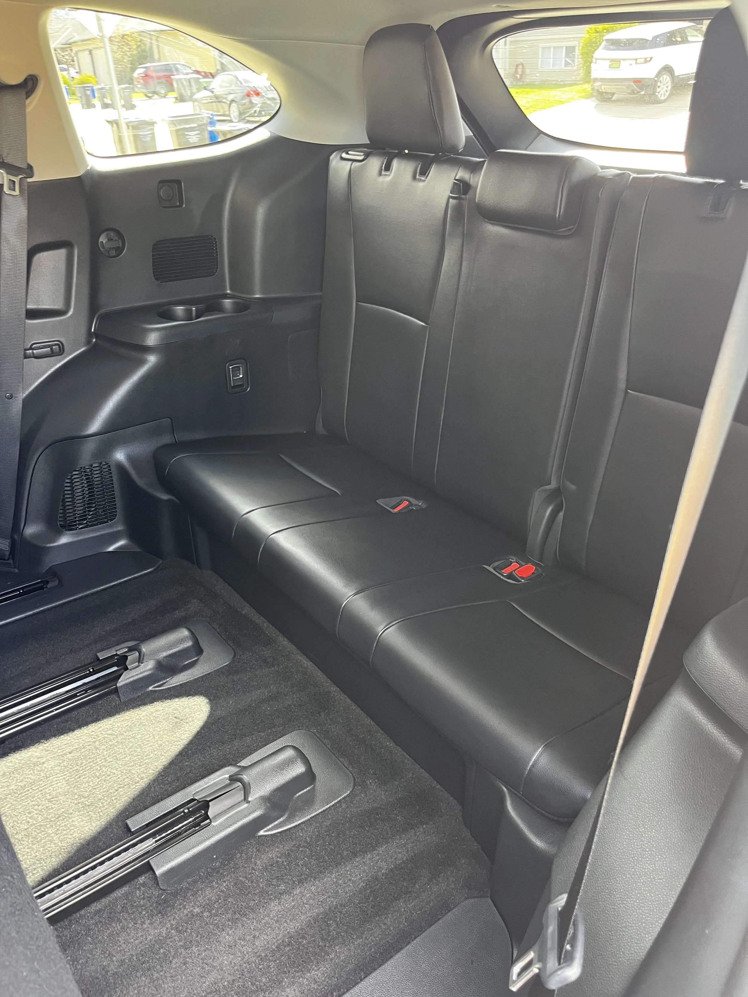 The backseat of a car with black leather seats, showing the second row of seats with seat belts, a window, and part of the trunk space.