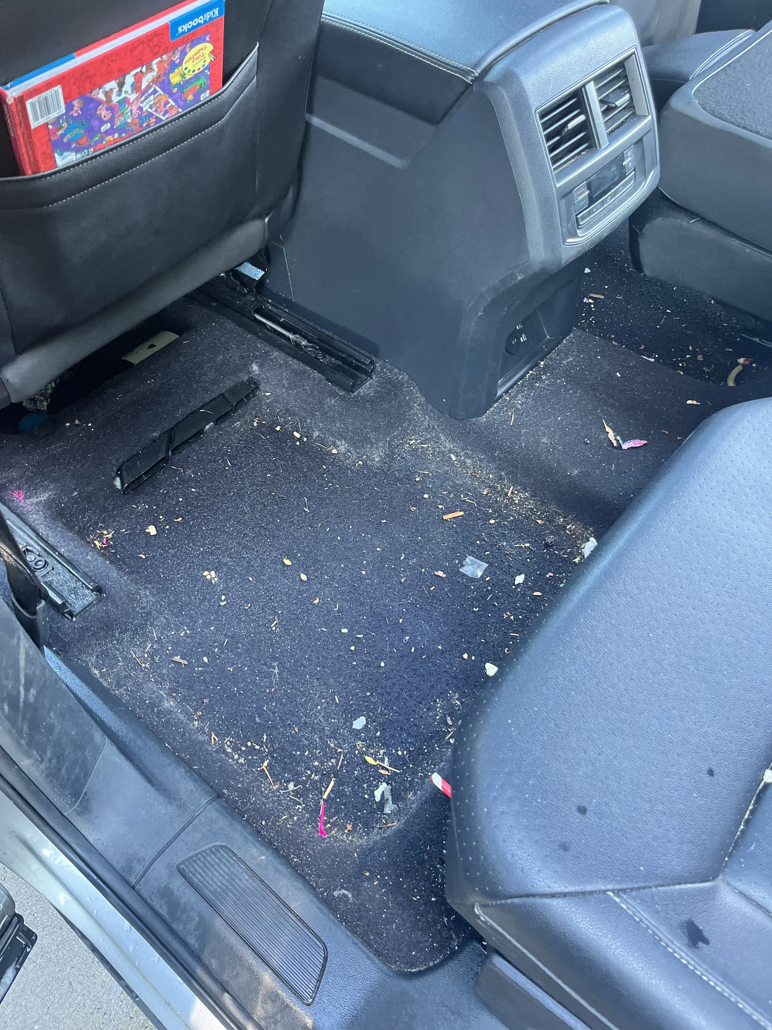 The back seat area of a car with the floor dirty and scattered with crumbs, trash, and debris.