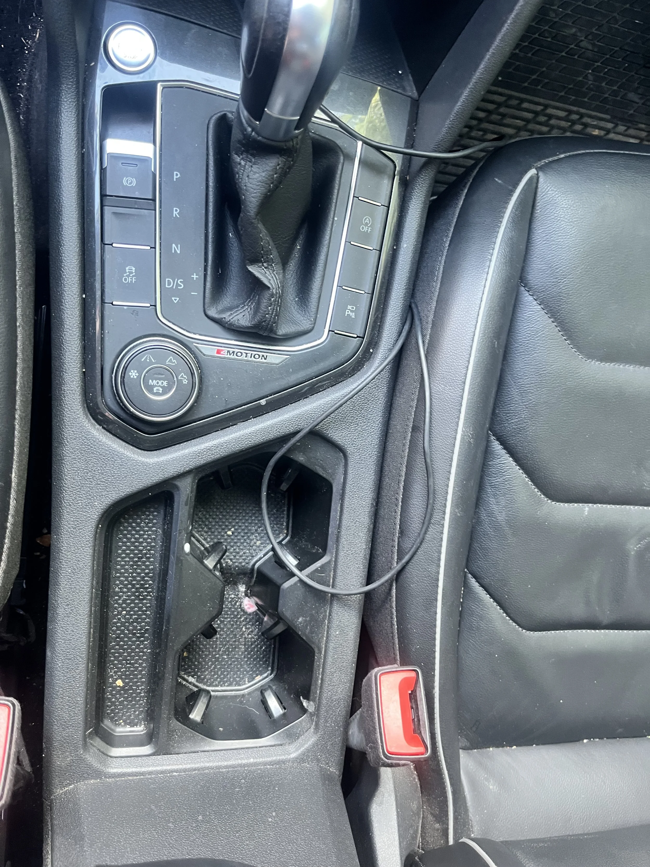 Center console of a vehicle with gear shifter, empty cup holder, and various control buttons and switches.