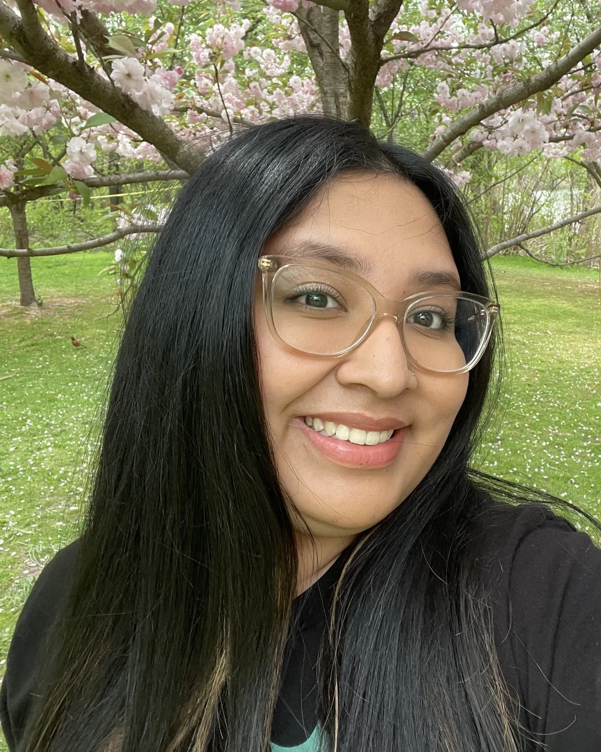 Woman with glasses smiling in front of cherry blossom tree.