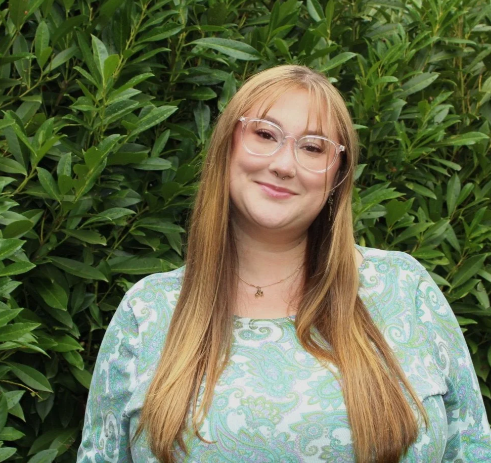 Person blonde hair glasses standing in front of bush