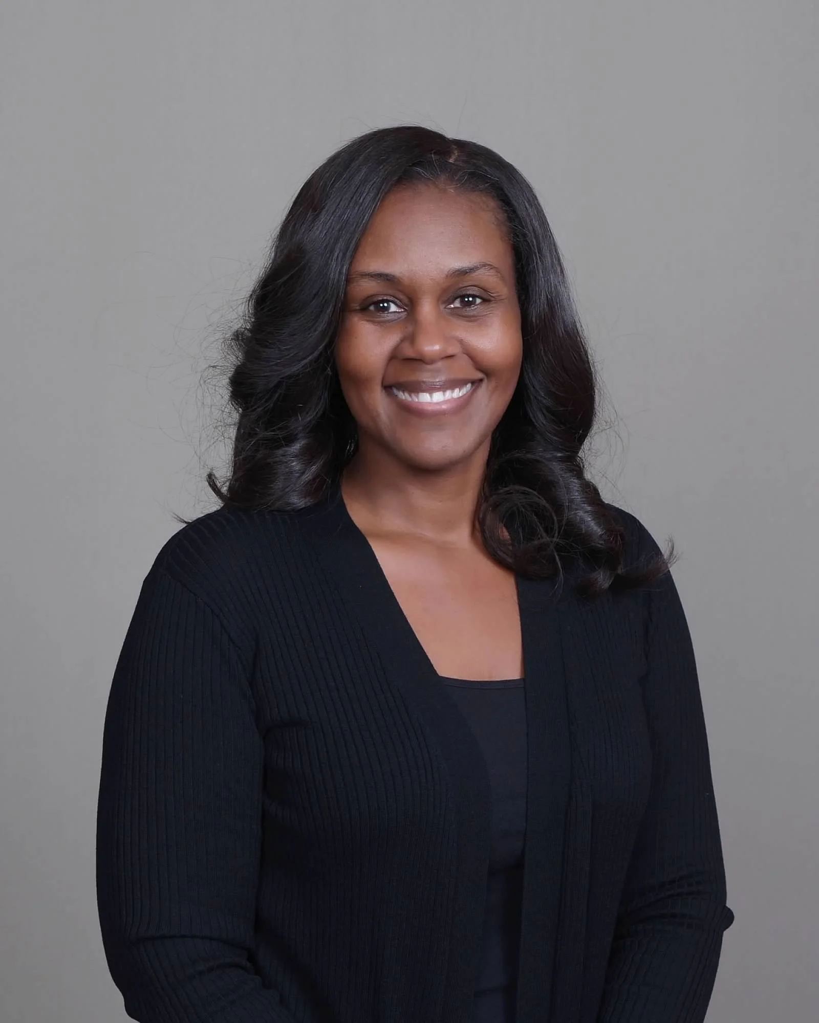 Woman with long wavy black hair smiling at the camera against a plain background.