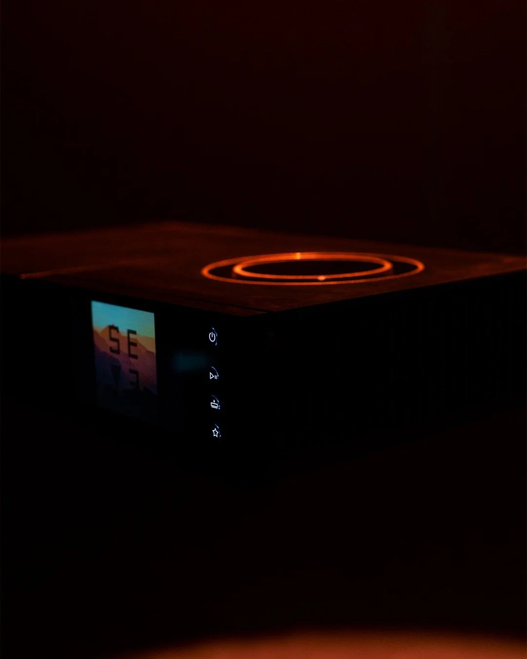 Digital cooking appliance with a small colorful screen and illuminated control buttons, glowing with an orange heat ring on top.