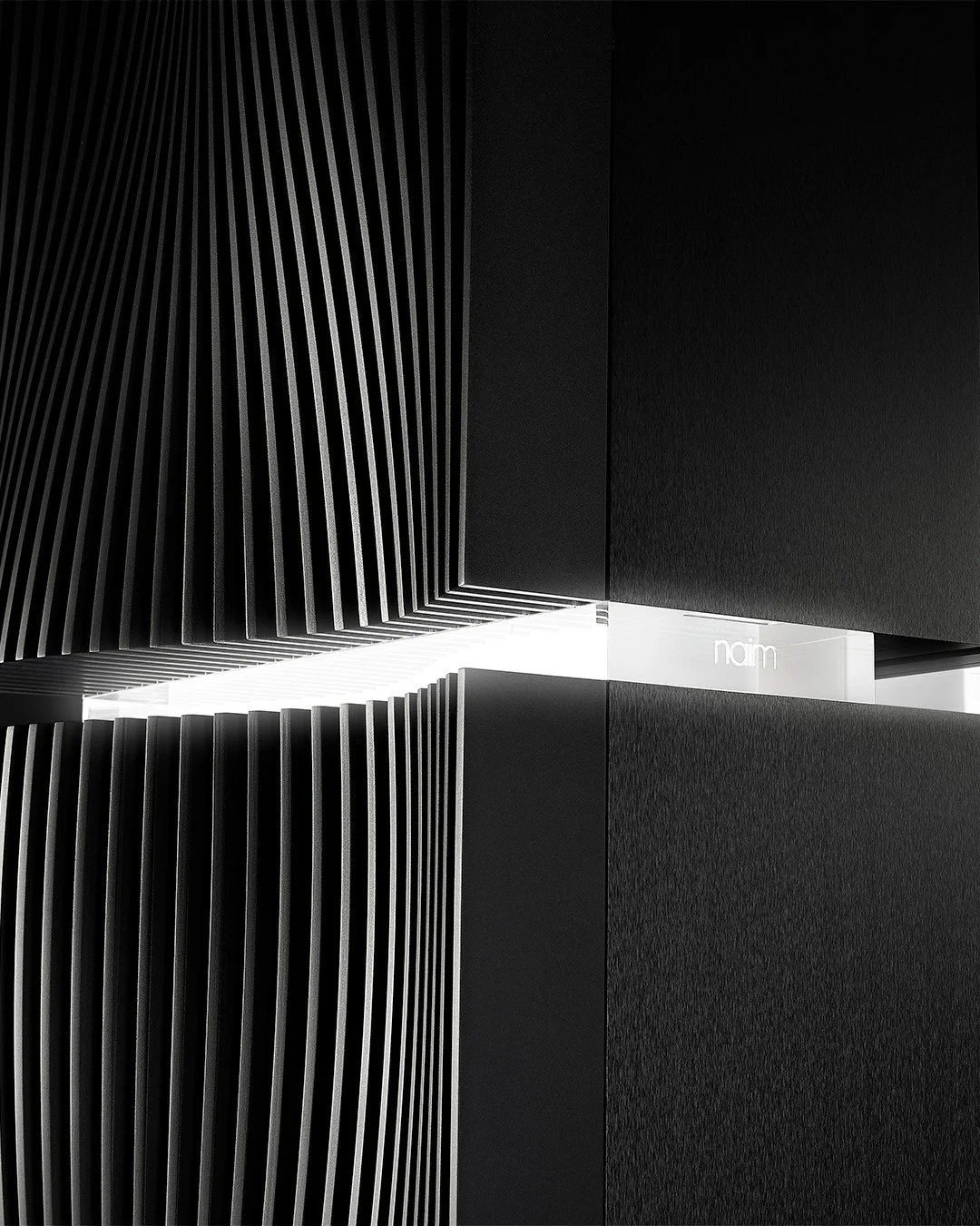 Modern black and white interior with geometric design, featuring slatted walls and a hidden light source, with the word 'naim' visible.