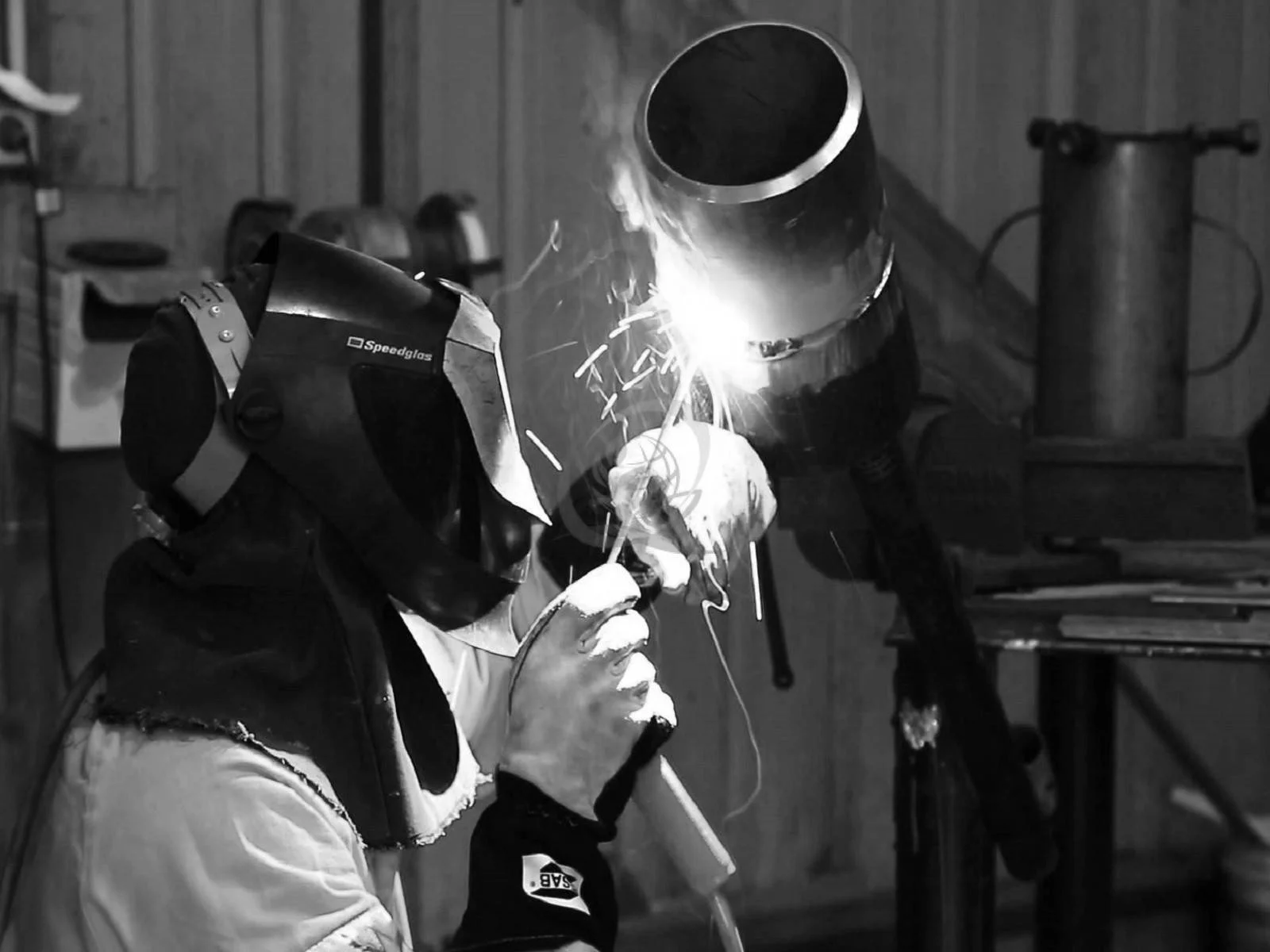 A person welding metal with a welding helmet and gloves in a workshop, sparks flying from the welding process.