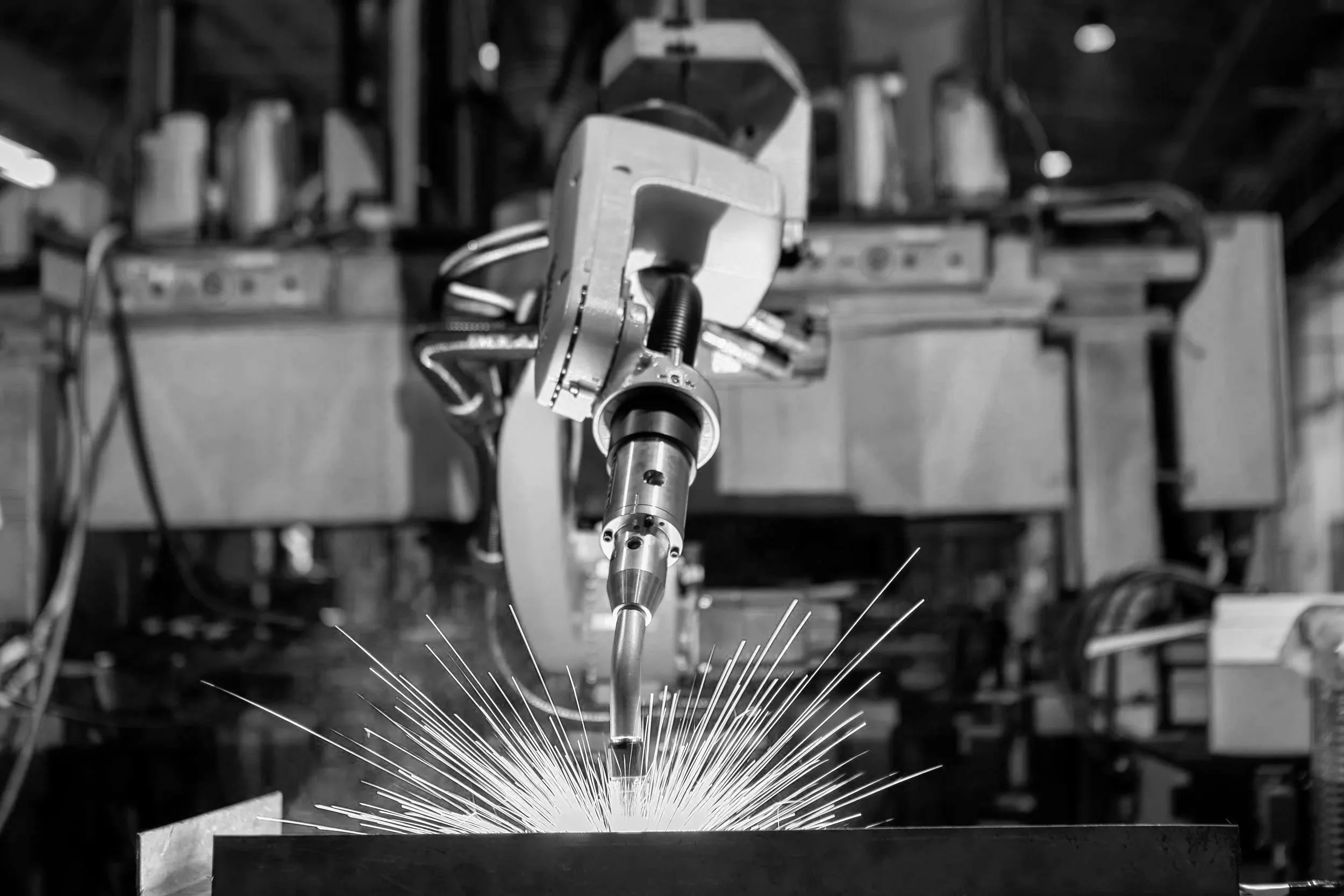 a robotic welding arm sparks as it welds a metal piece in an industrial workshop