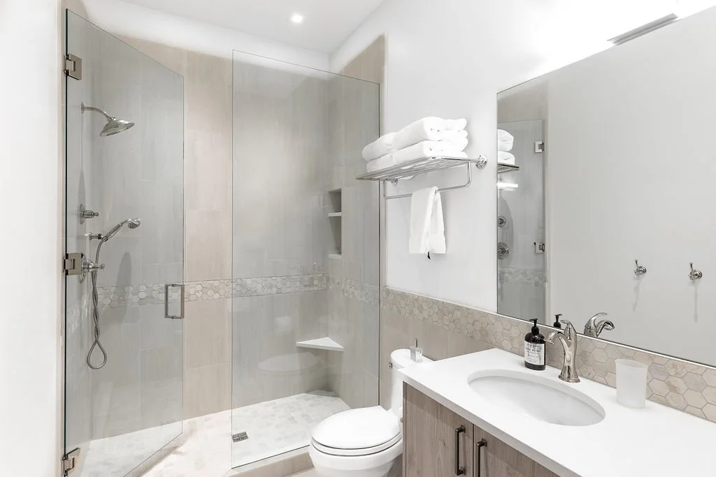 Modern bathroom with walk-in shower, glass doors, white towels, and vanity with sink and toiletries.