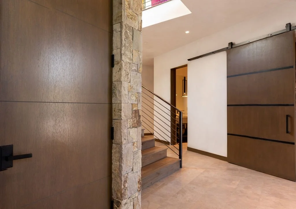 Modern interior with stone wall, wooden sliding doors, staircase with metal railing, and neutral-colored walls and flooring.