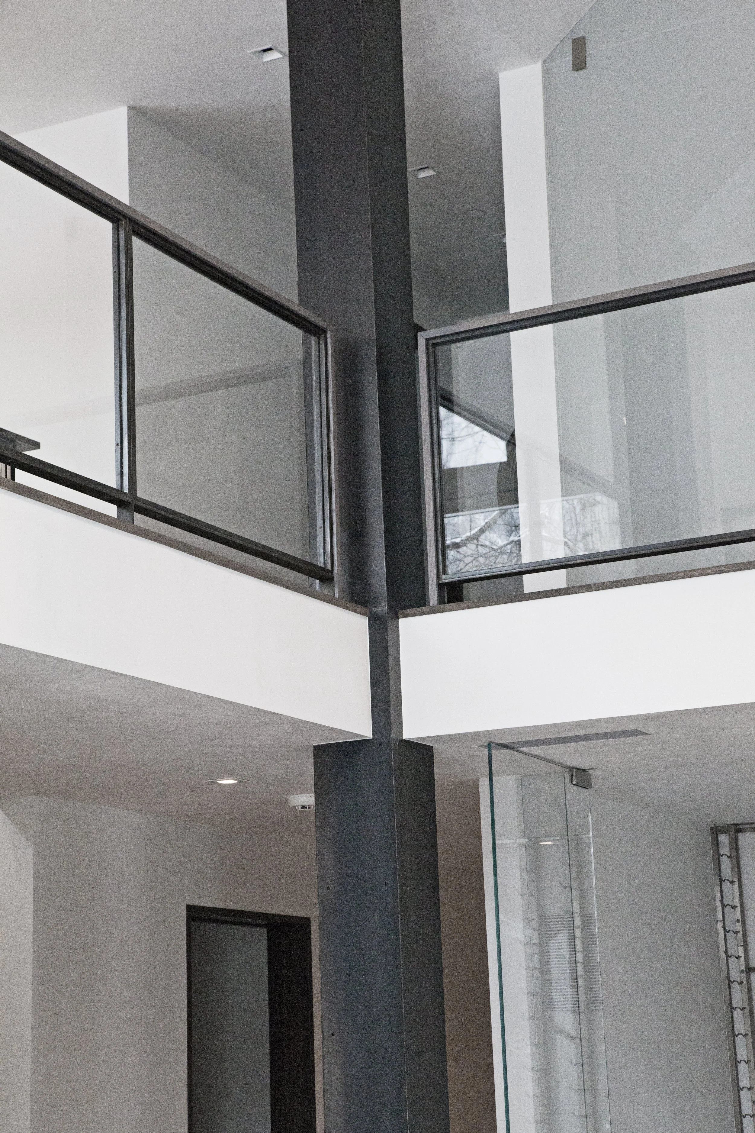 Interior view of a modern building with a black vertical support beam, glass railings, and white walls.