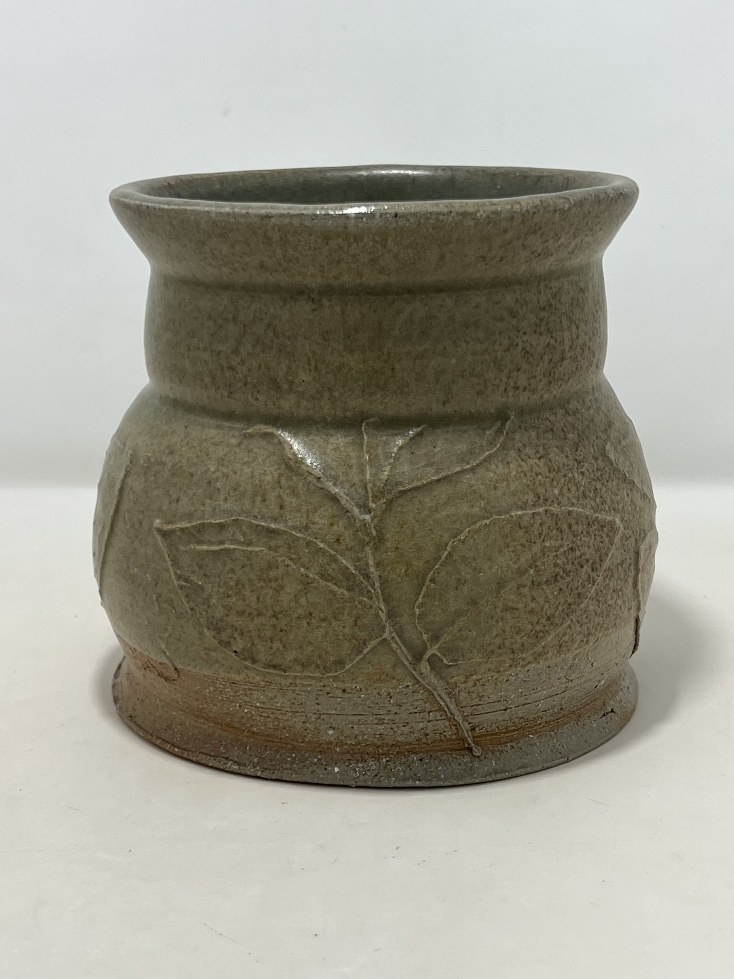 A ceramic vase with a leaf carved into its surface, featuring a rough, natural texture and earthy tones.