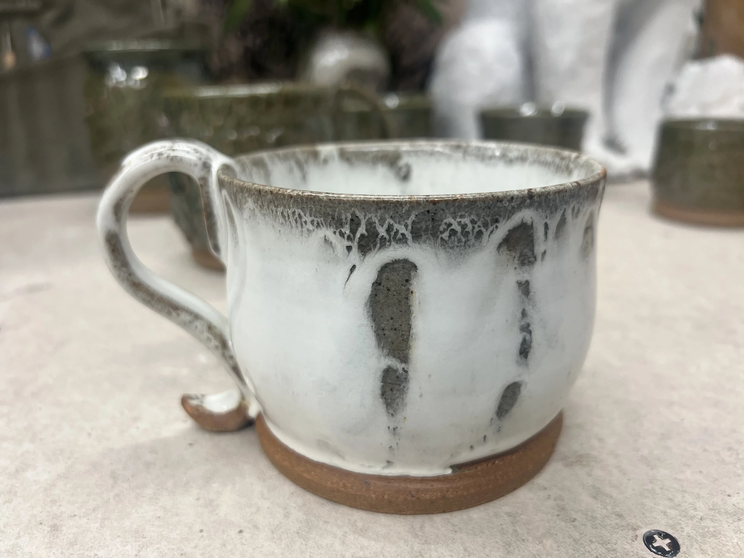 A ceramic mug with black and white glaze patterns, sitting on a round wooden coaster on a light-colored surface.