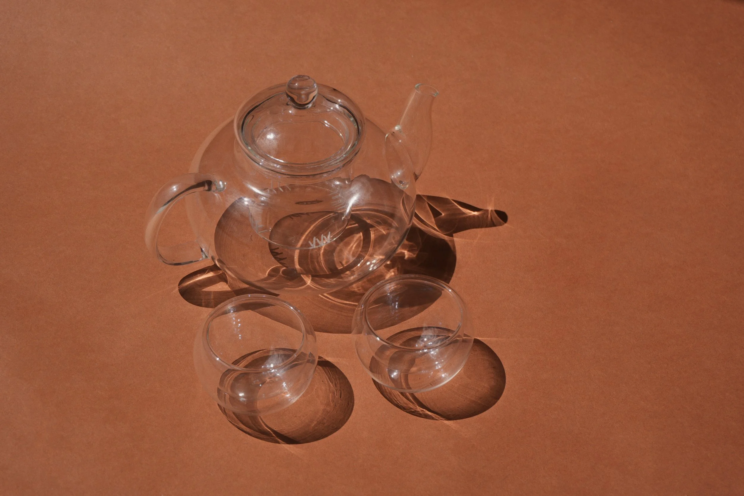 Clear glass teapot and cups on a brown surface casting shadows
